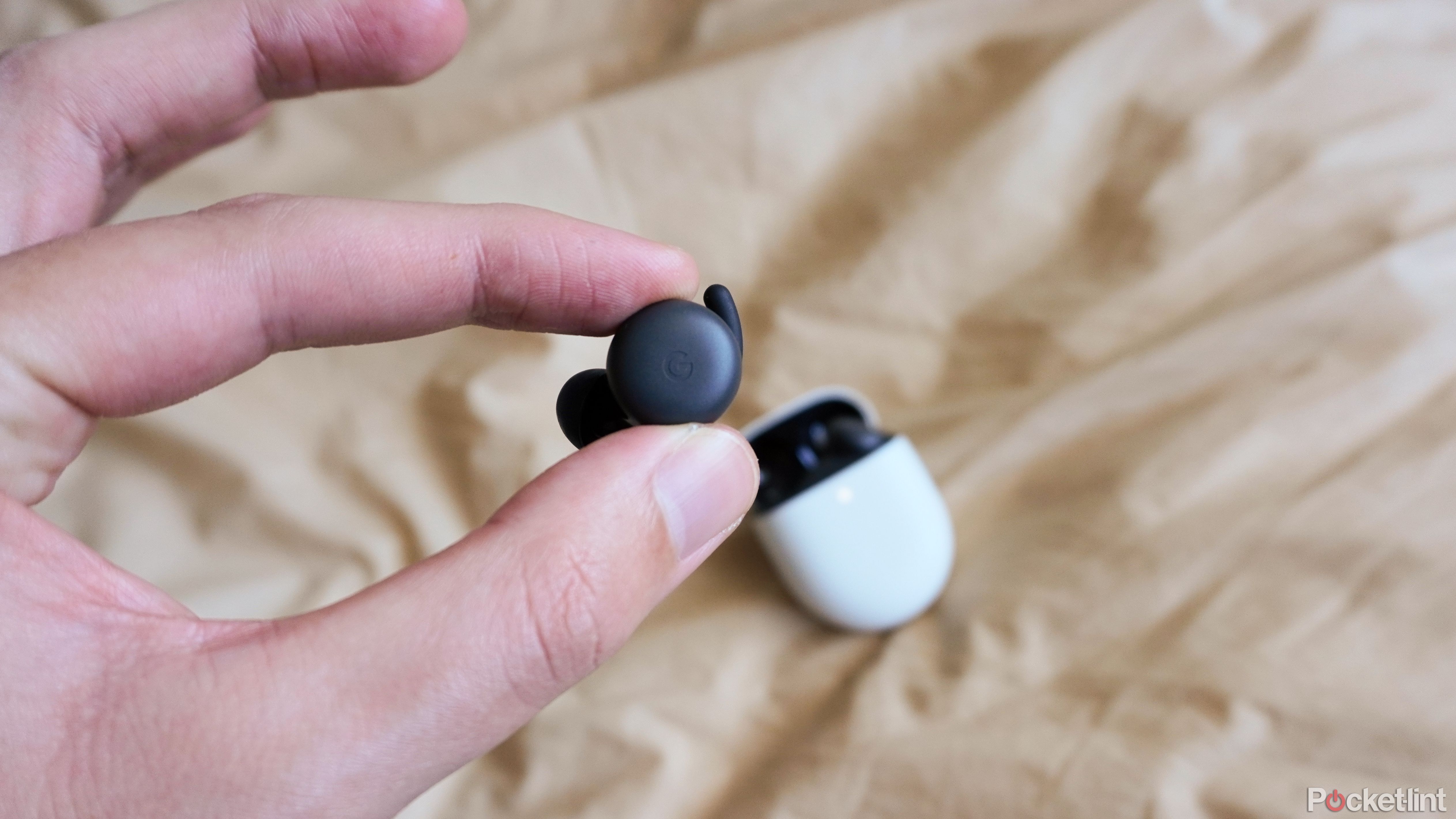 An earbud being held in front of the Pixel Buds A-Series charging case.