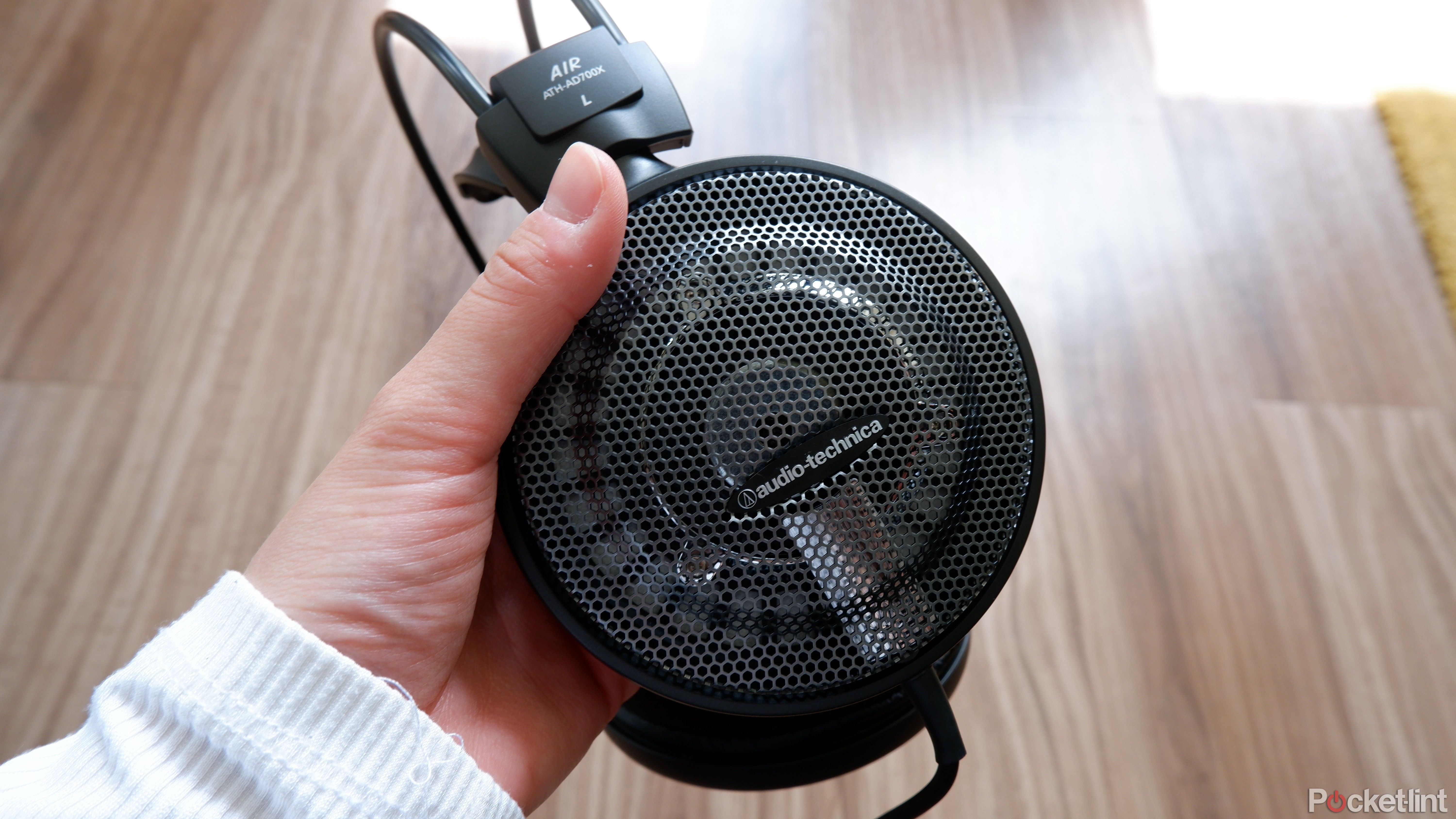 The Audio-Technica ATH-AD700X ear cup being held in a hand above a wooden surface