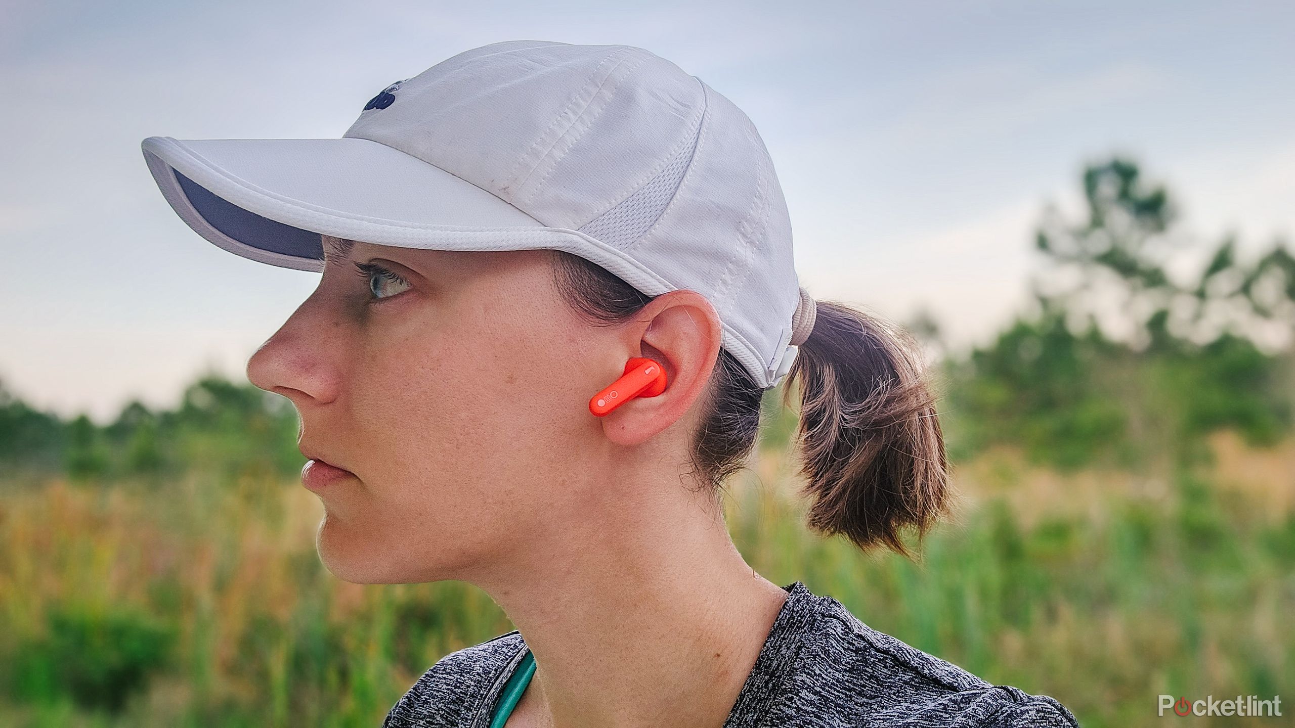 A woman's head from the side with the orange CMF Buds in her ear.