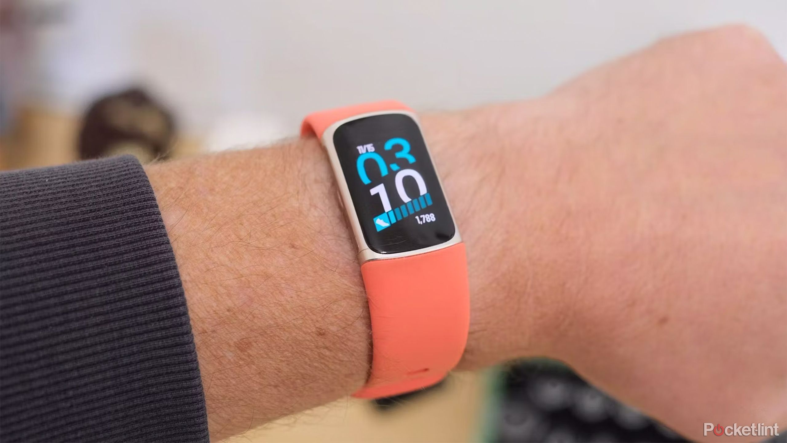 The orange Fitbit Charge 6 on a wrist in front of a blurred background. 