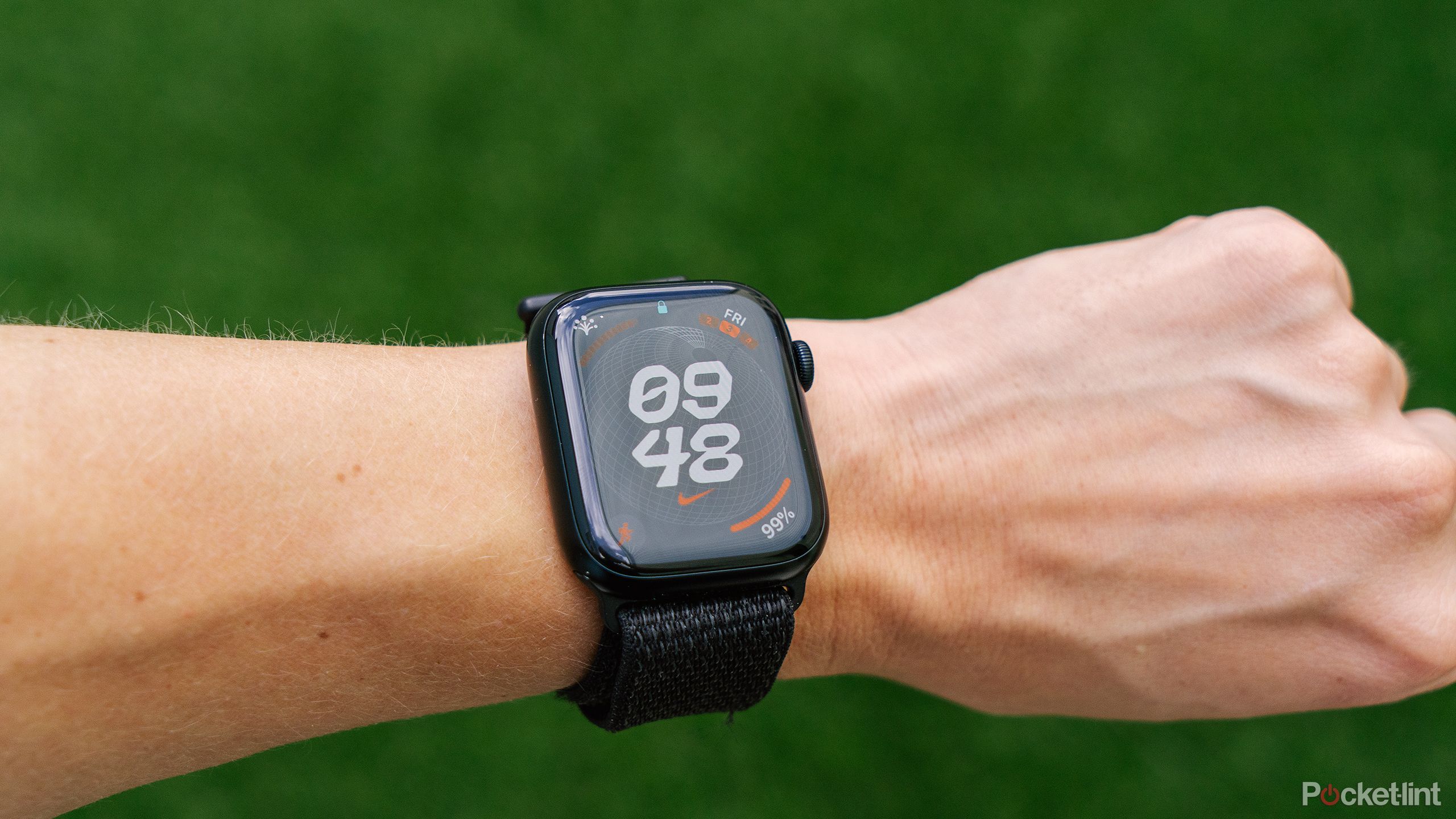 The Apple Watch on a wrist in front of a blurred green background. 