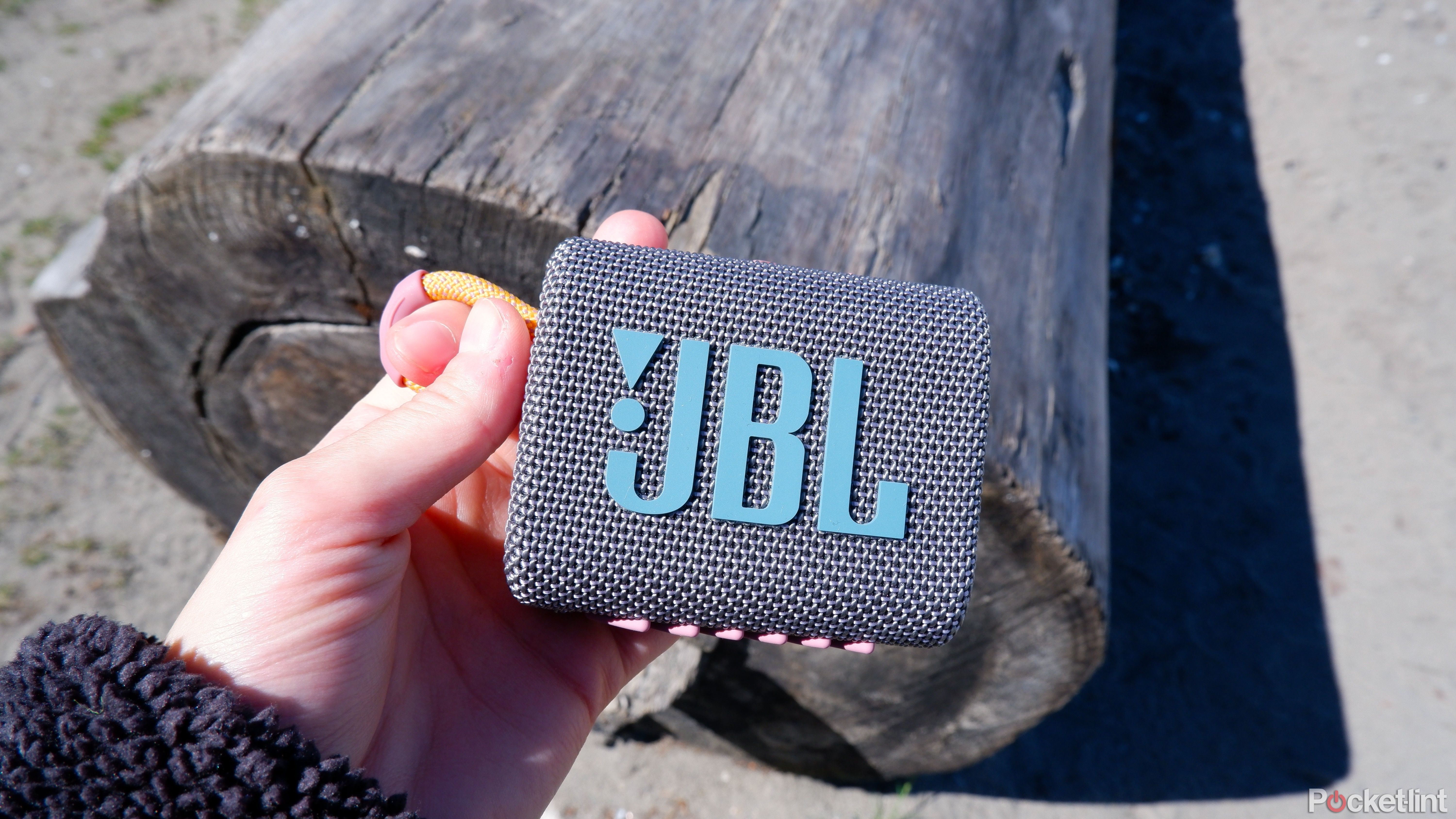 JBL go 3 being held in a hand in front of a log on the beach