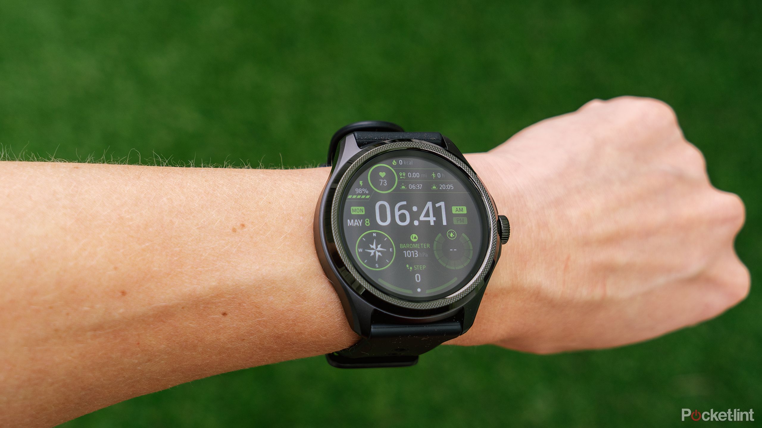 The Mobvoi TicWatch Pro 5 smartwatch on a wrist in front of a blurred green background.
