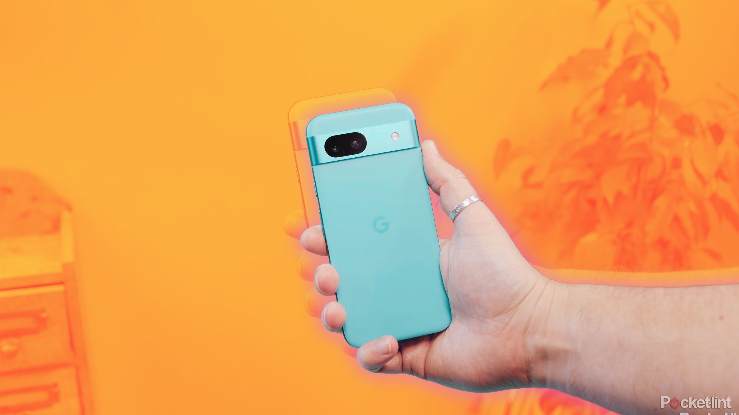 A blue Pixel 8a in hand against an orange background. 