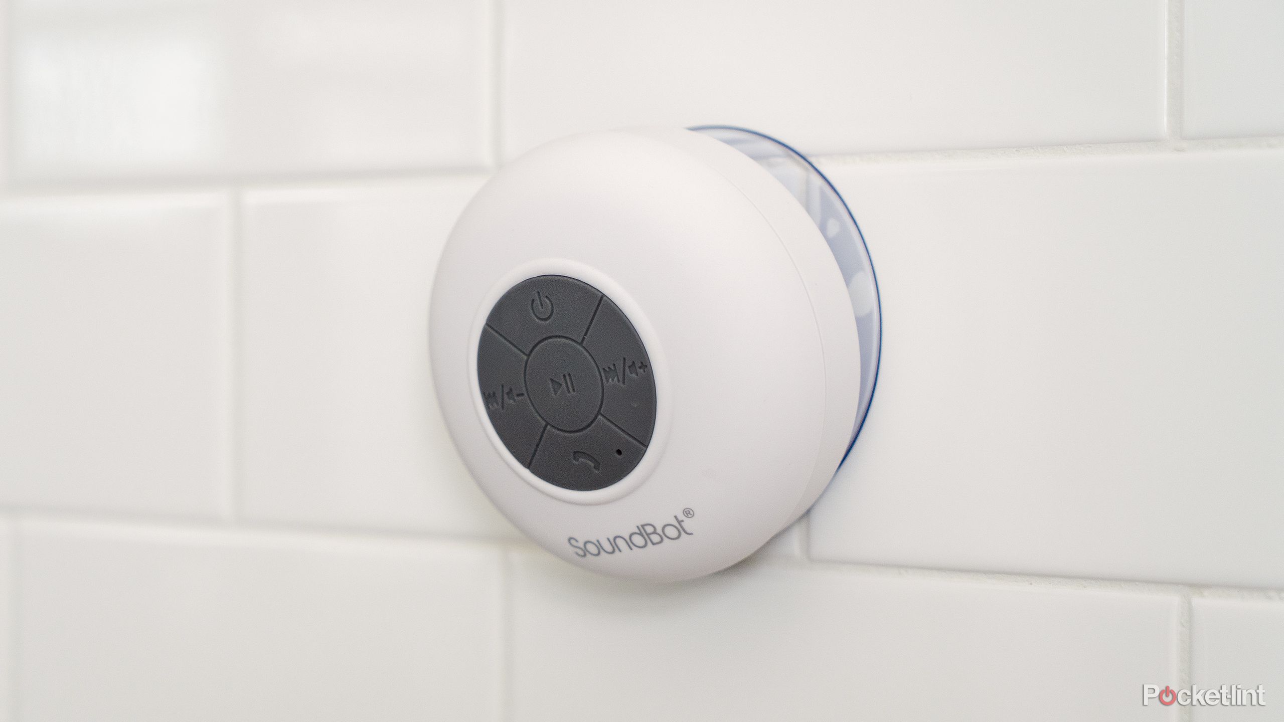 The white Soundbot SB510 speaker on a white tile shower wall.
