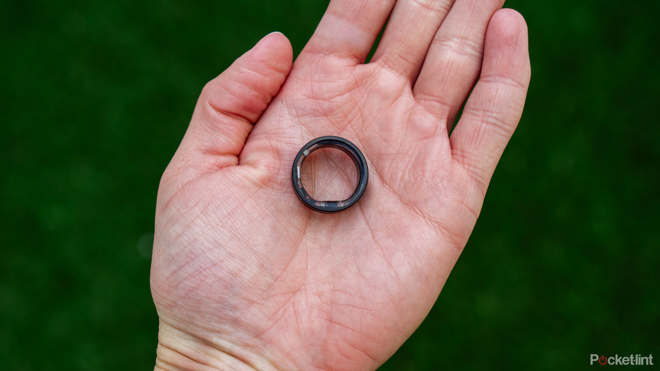 The Ultrahuman Ring Air sits on an open palm above a blurred green background. 