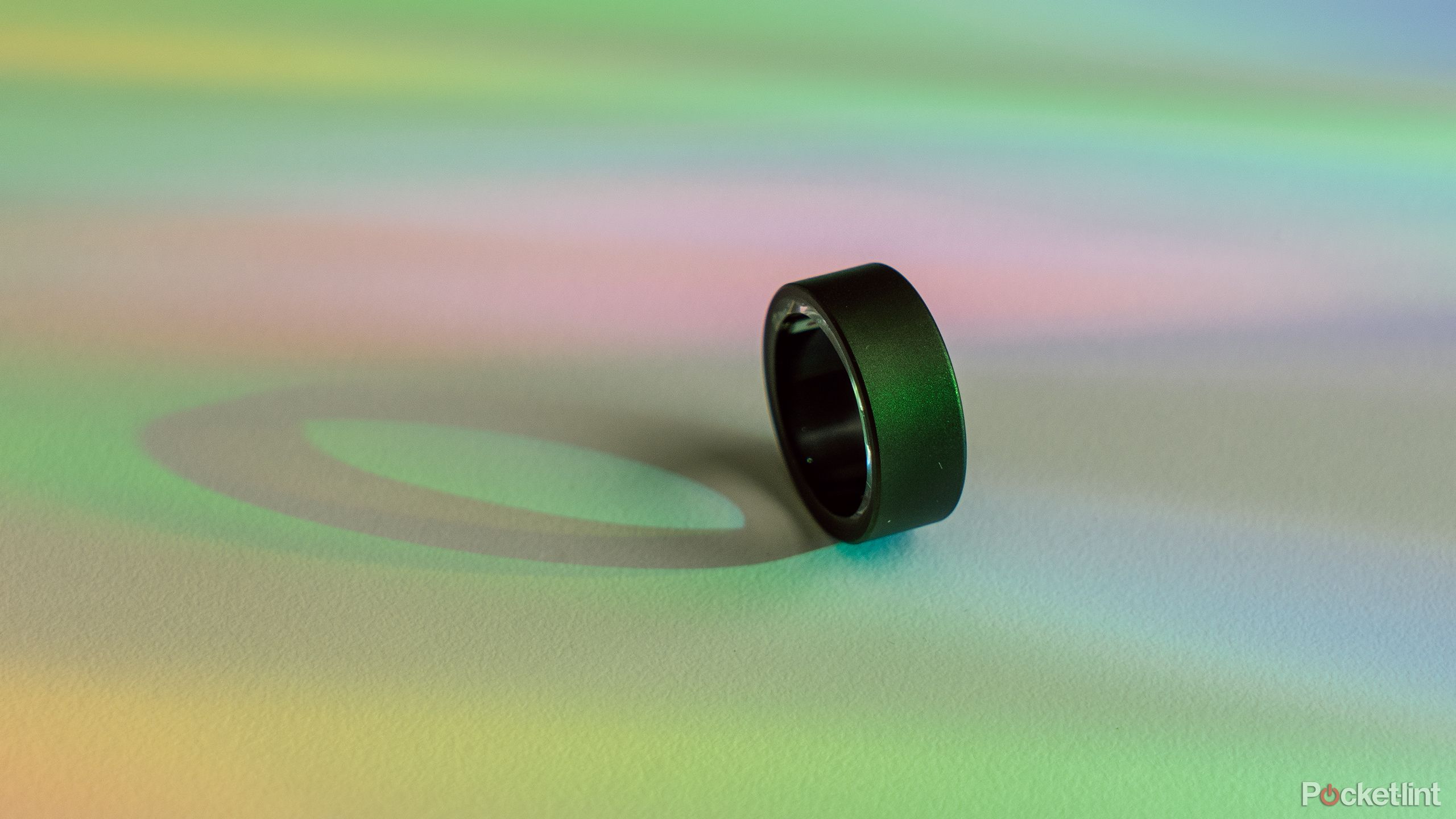 The Ultrahuman Ring Air on its side on a white desk with rainbow light. 