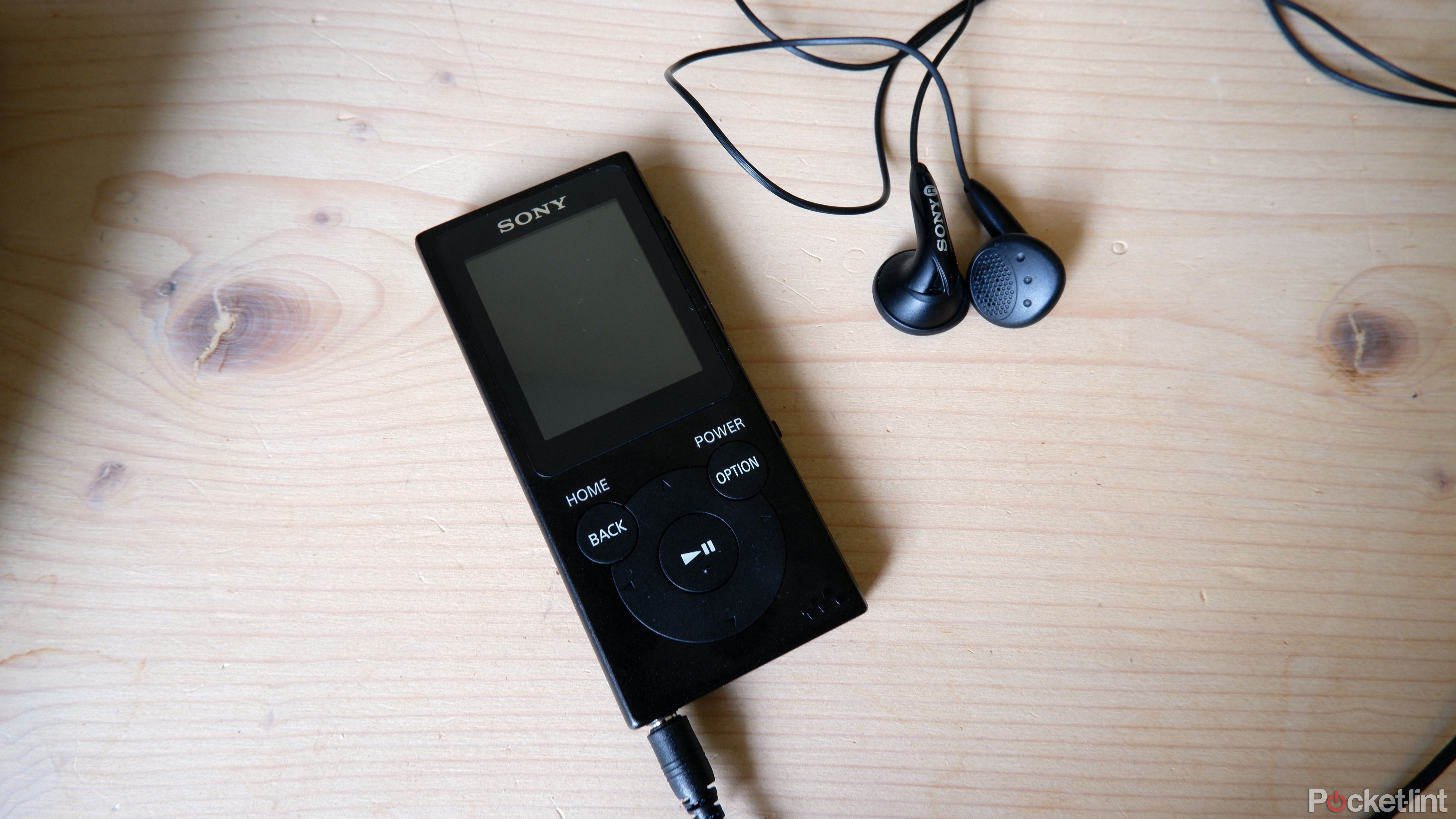 A Sony Walkman on a wooden table with the earbuds plugged in.