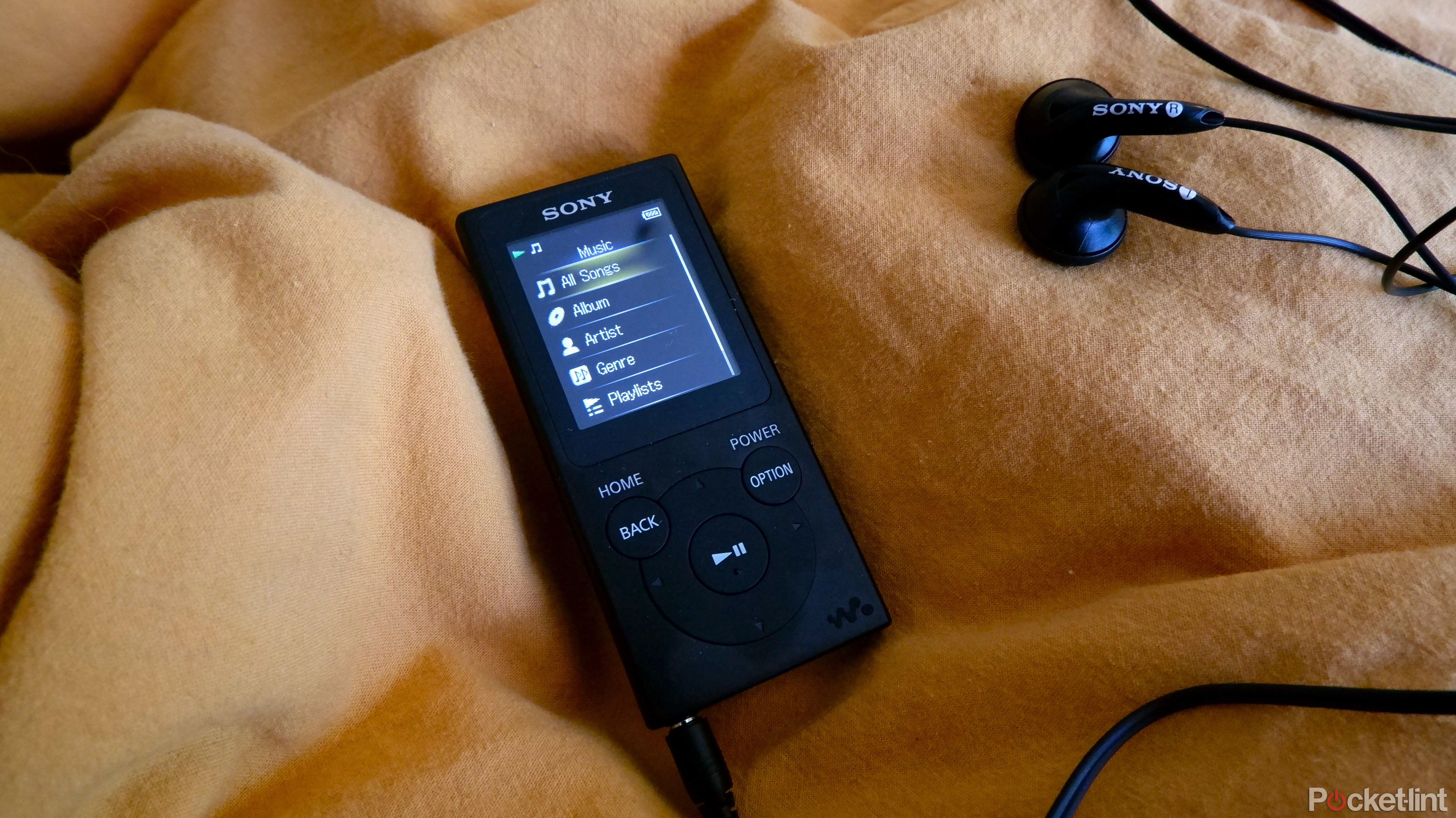 A Sony Walkman resting on a yellow sheet with the earbuds plugged in, showing the music menu.