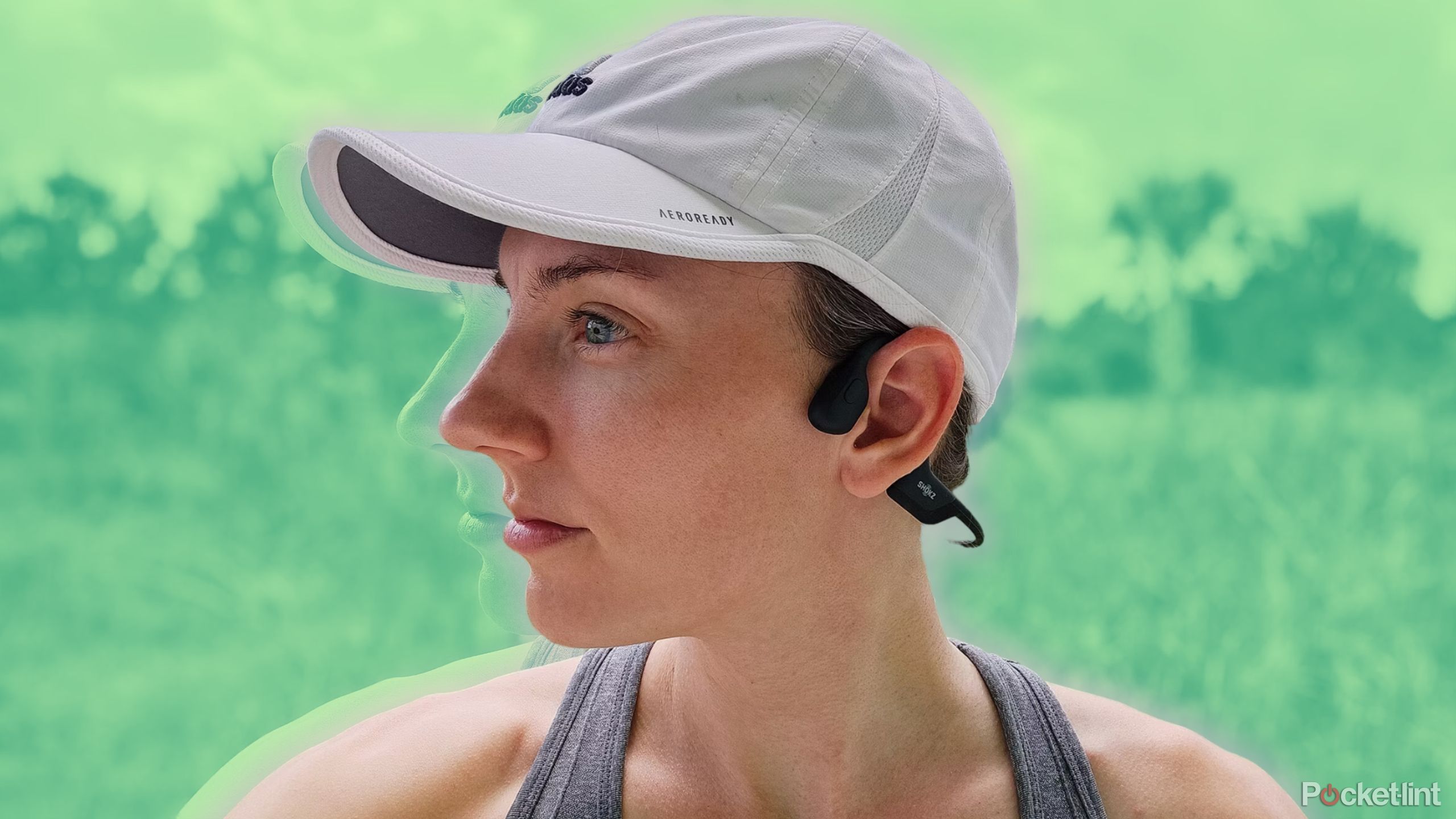 A woman with a white running hat wears a pair of Shokz Open Run Pro bone conduction headphones in front of a blurred out forest background. 