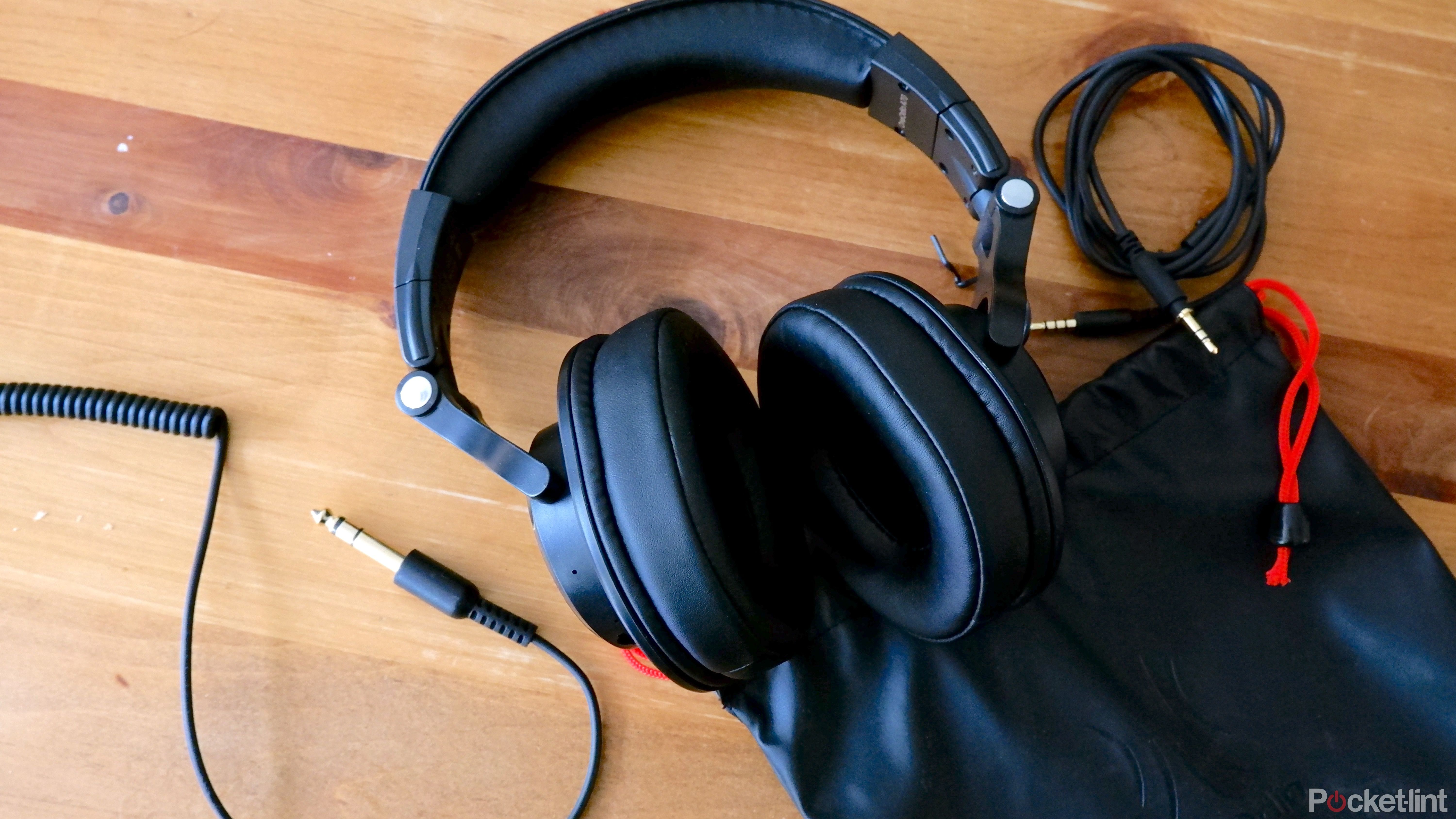 The OneOdio A70 headphones on a wooden coffee table next to the fabric case and both cables it comes with.