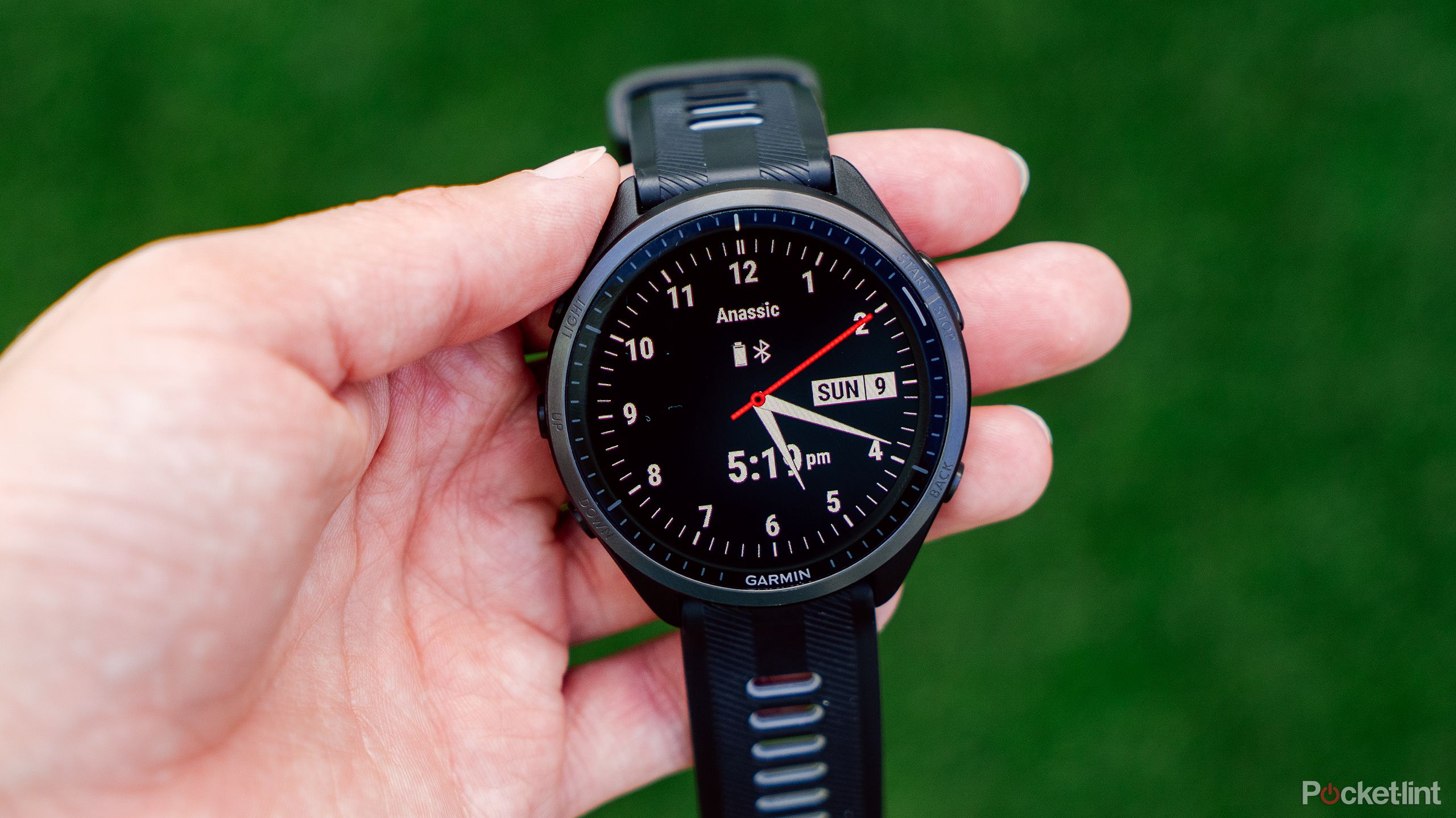 A hand holding the Garmin Forerunner 965 with an analog watch face. 