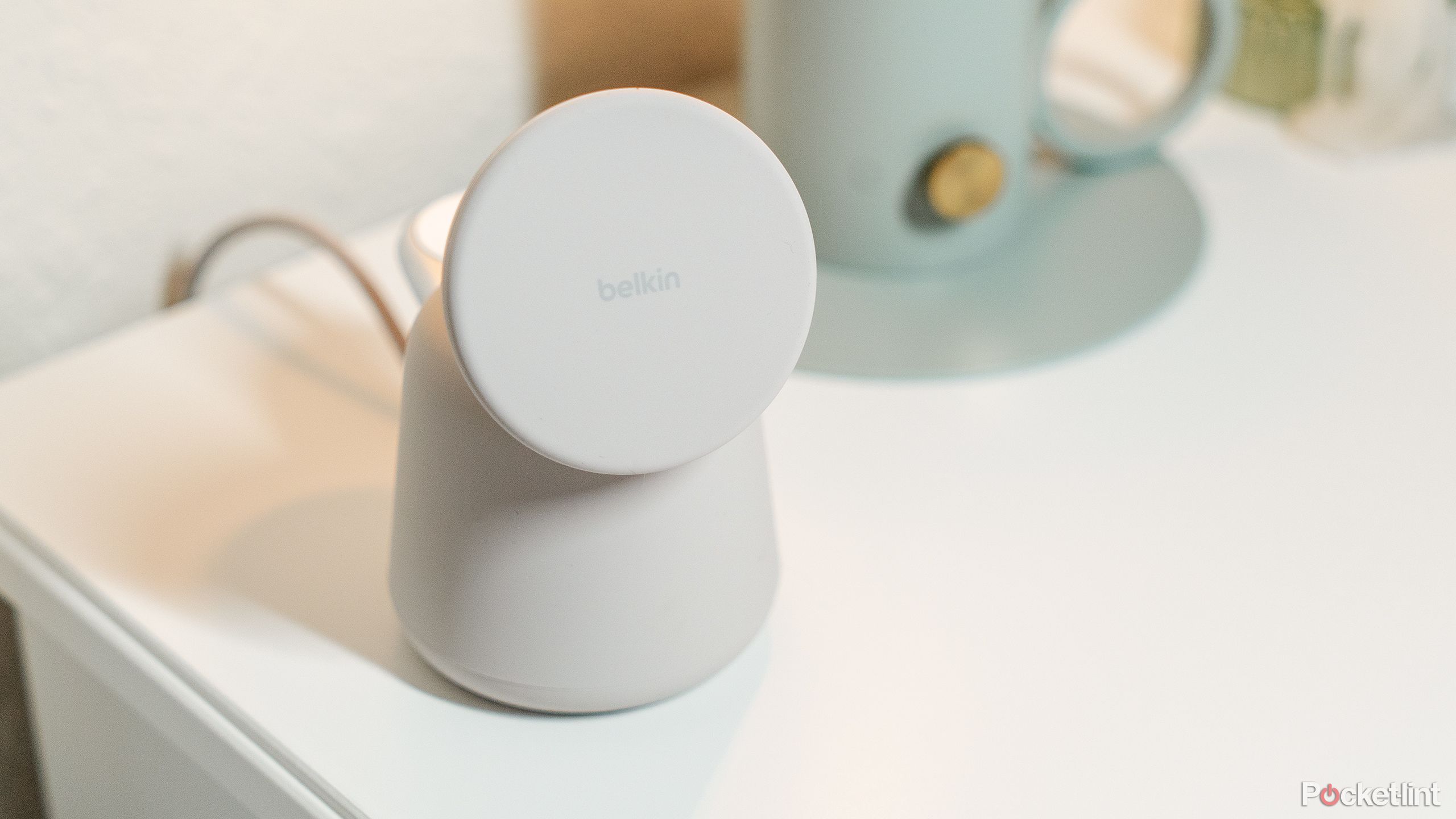 The Belkin BoostCharge PRO 2-in-1 Wireless Charging Dock on a white nightstand next to a green lamp.