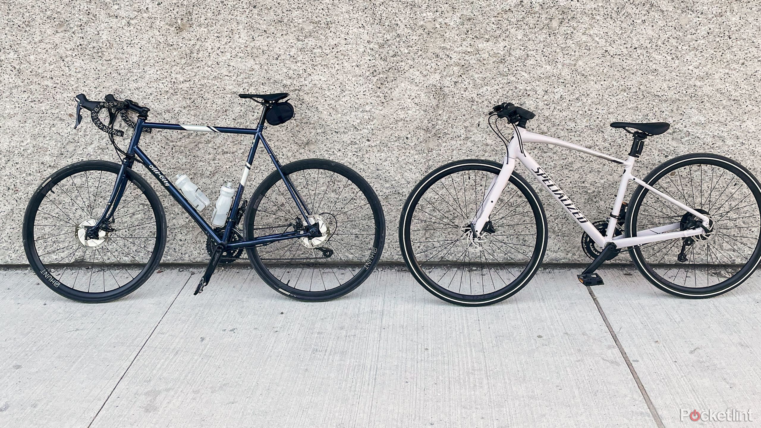 Two bikes stand against a concrete wall