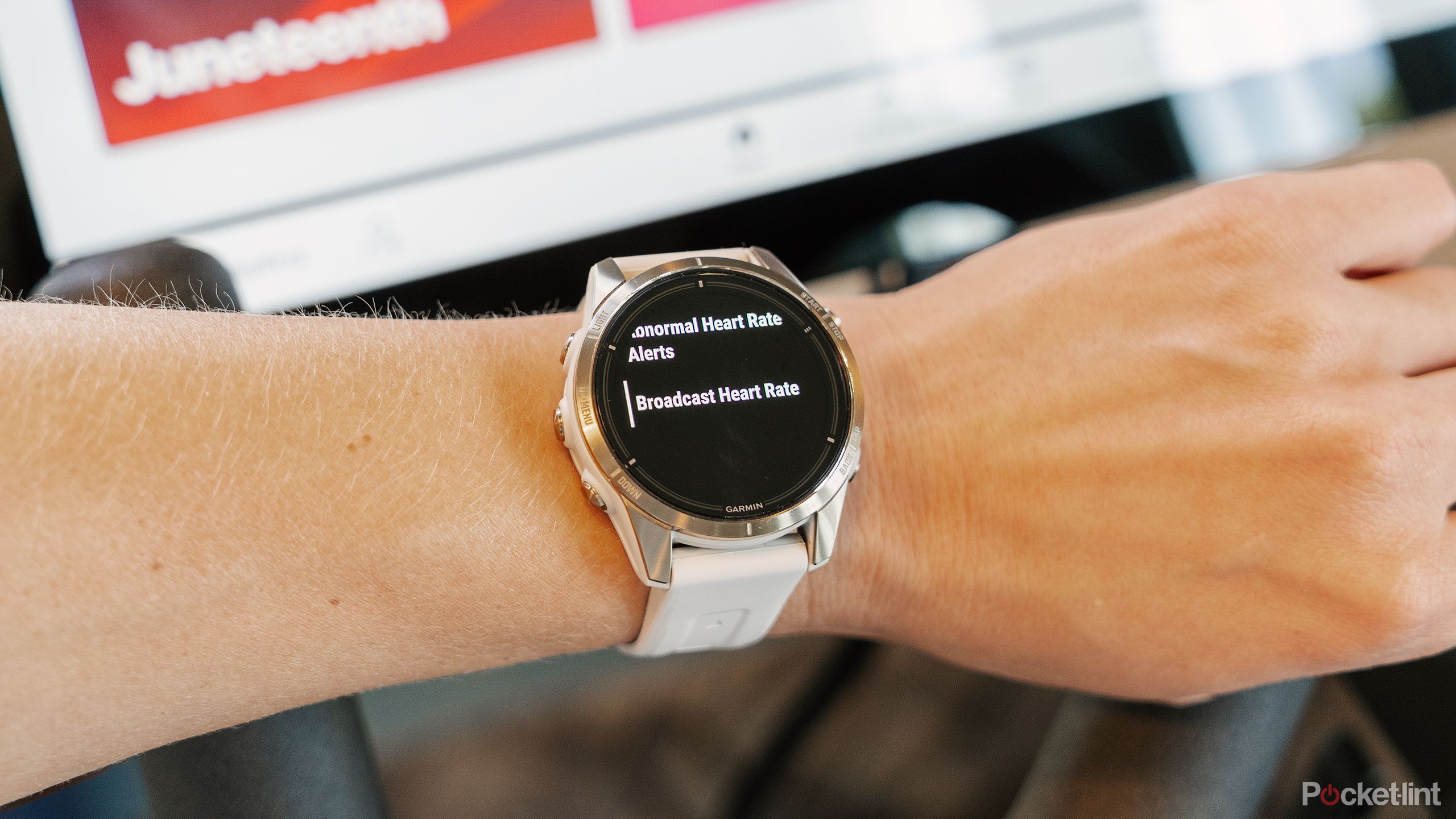 A wrist with a Garmin epix Pro Gen 2 Sapphire Edition is held in front of a Peloton screen.