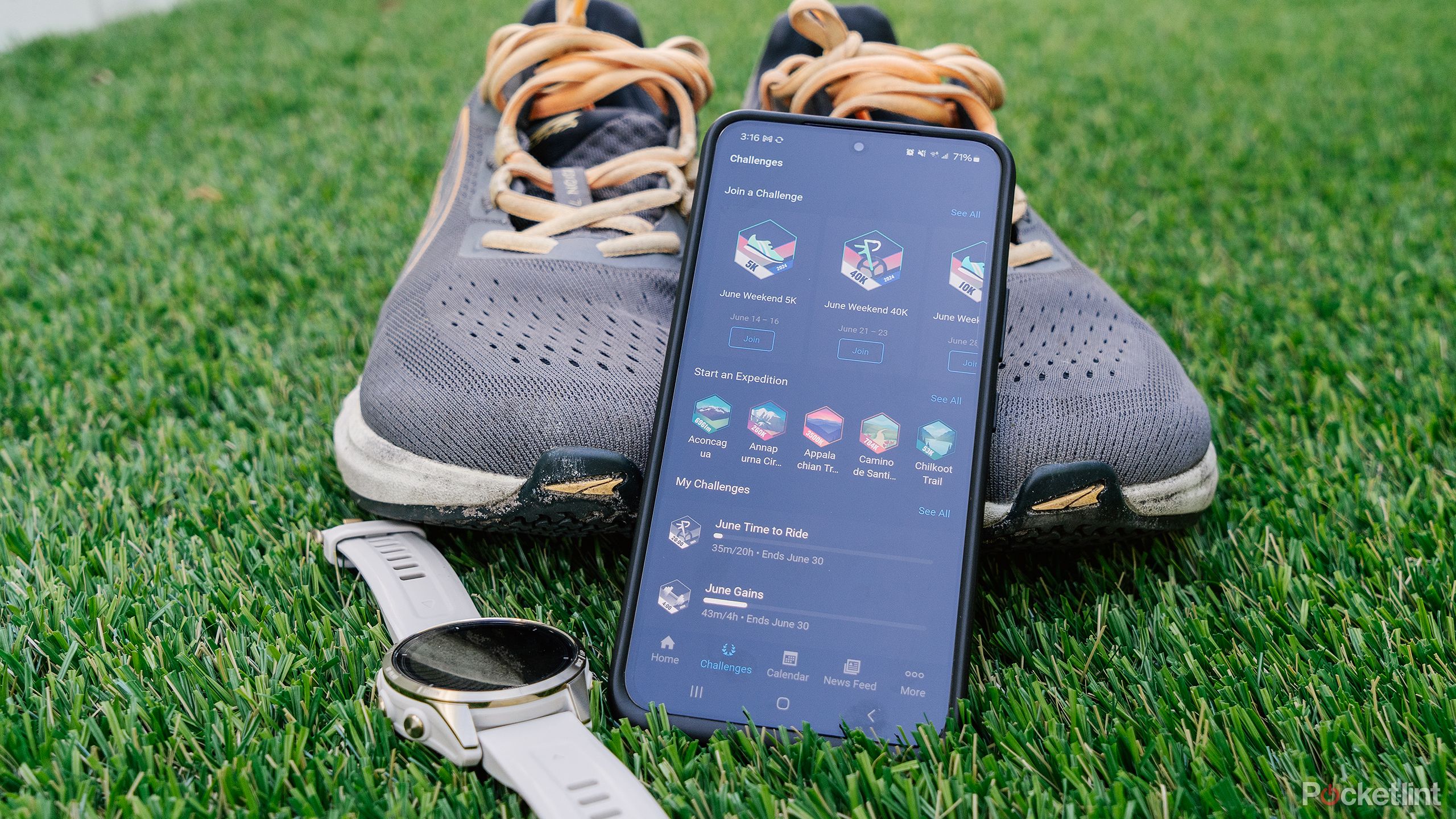 A phone with Garmin Challenges and Garmin epix Pro Gen 2 sit next to shoes on green turf. 