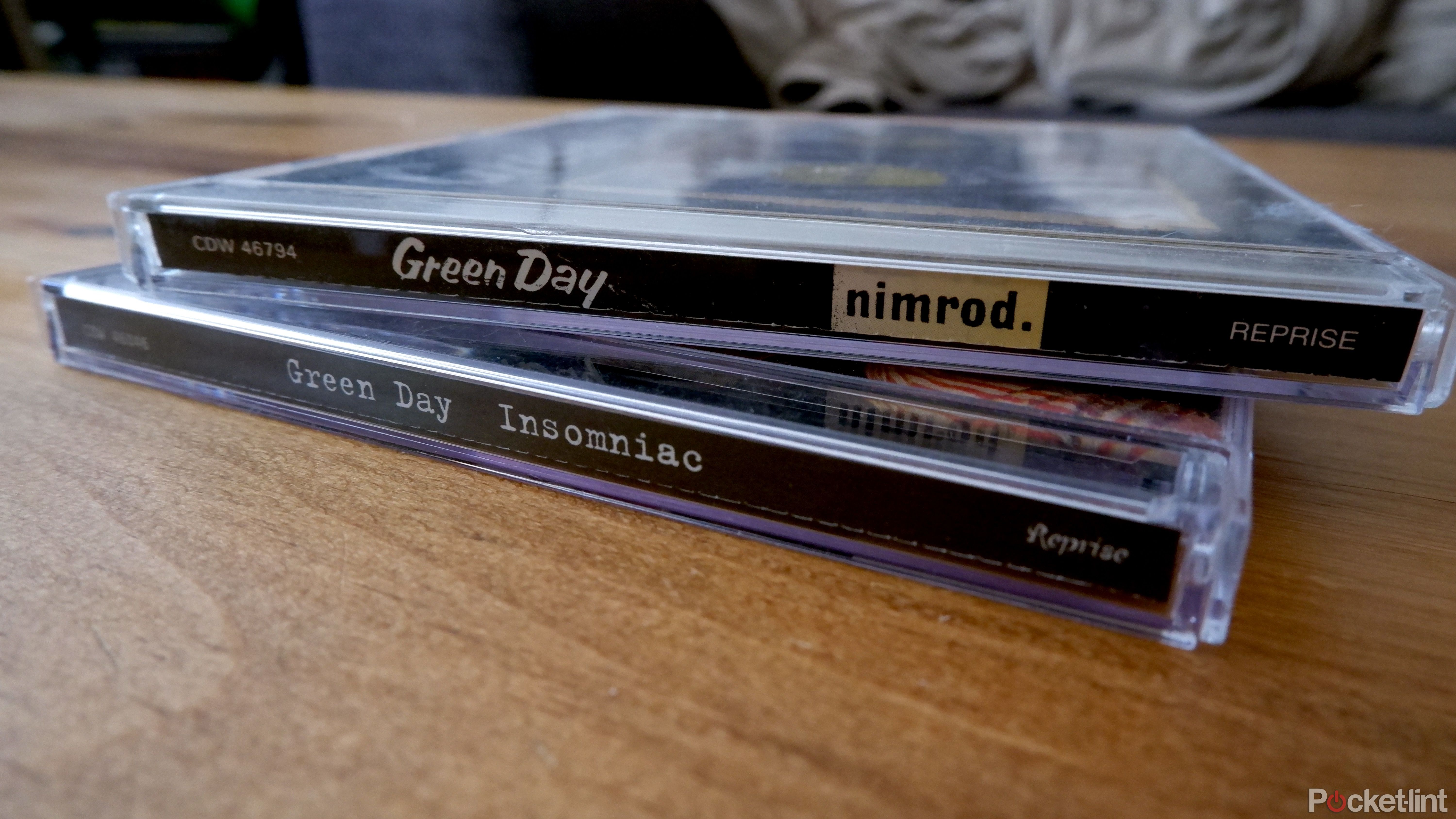 Two Green Day CD cases stacked upon one another on a wooden coffee table.