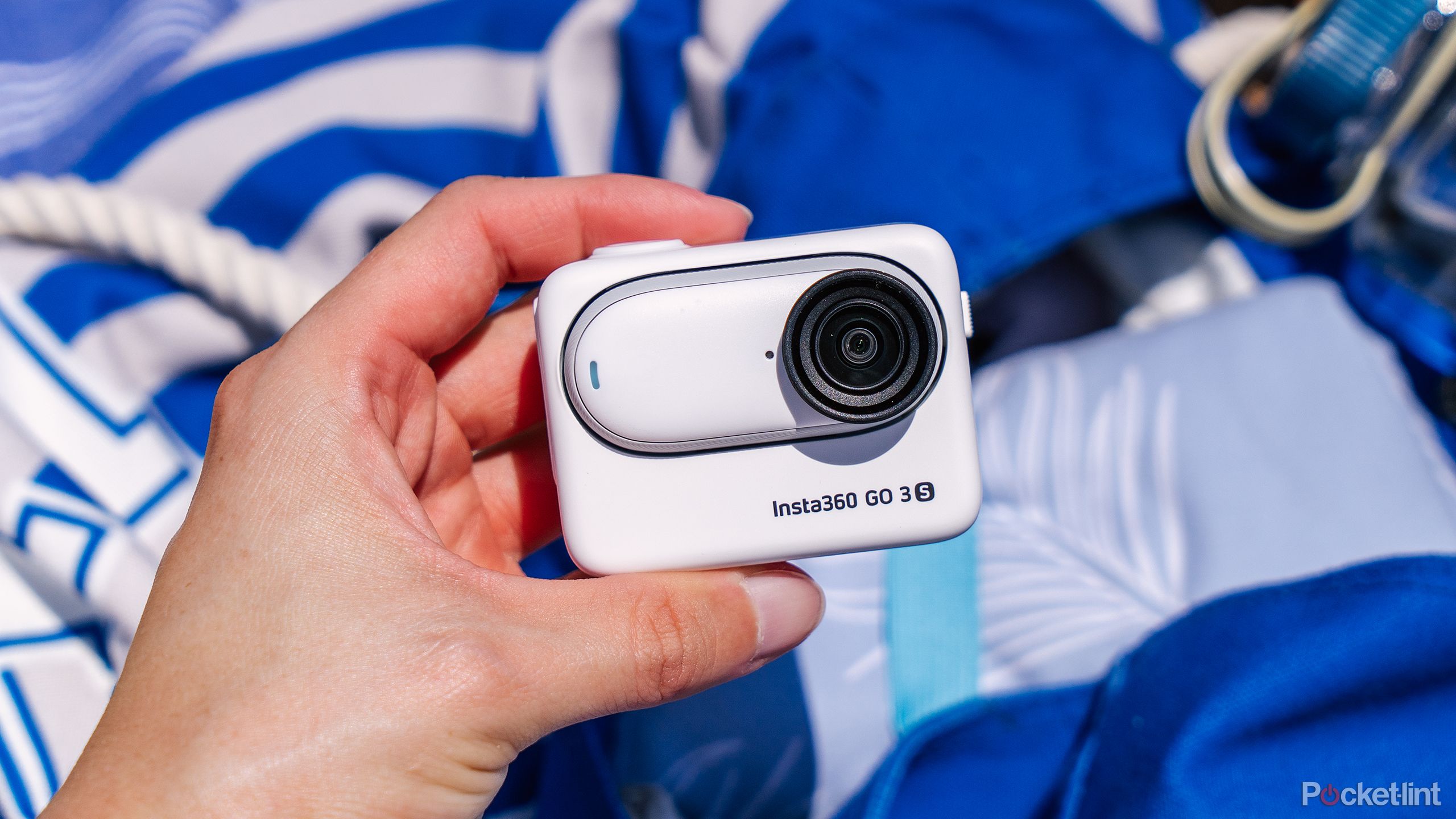 A hand holds the Insta360 GO 3S in the Actino Pod in front of a blue bag and towel.