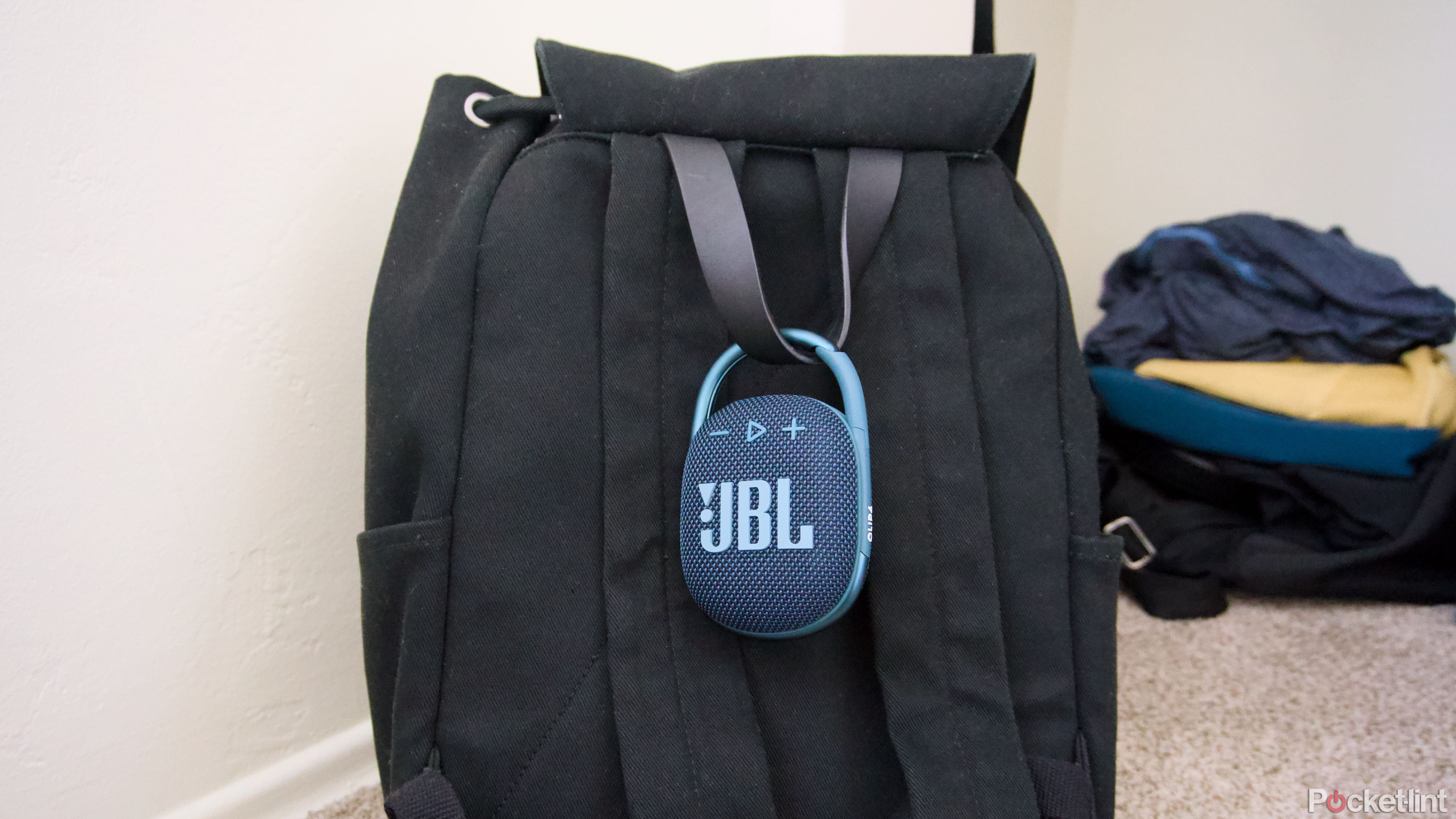 A JBL Clip 4 speaker attached to a black backpack.