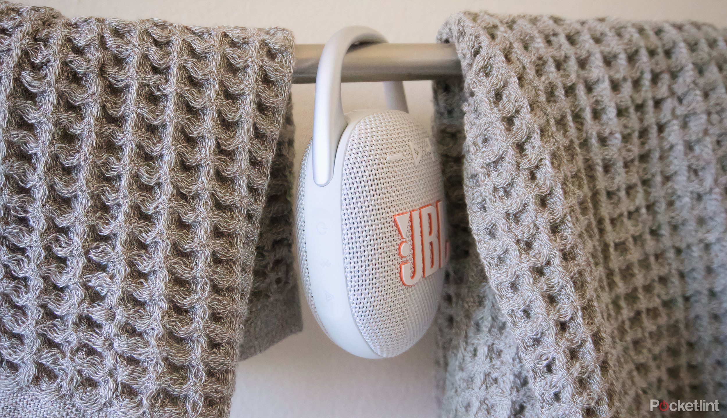 A JBL Clip 5 Bluetooth speaker hanging between hand towels.