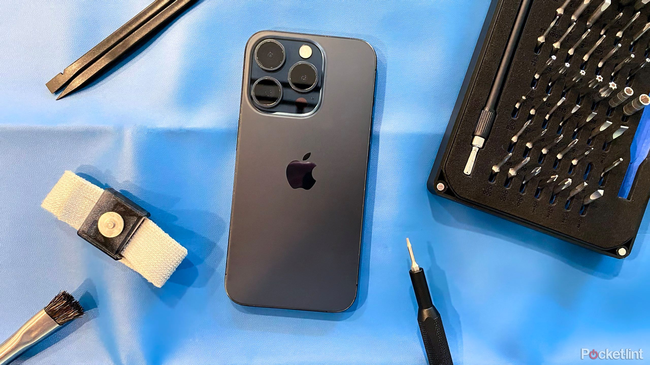 An iPhone 15 Pro on a blue mat with repair tools. 