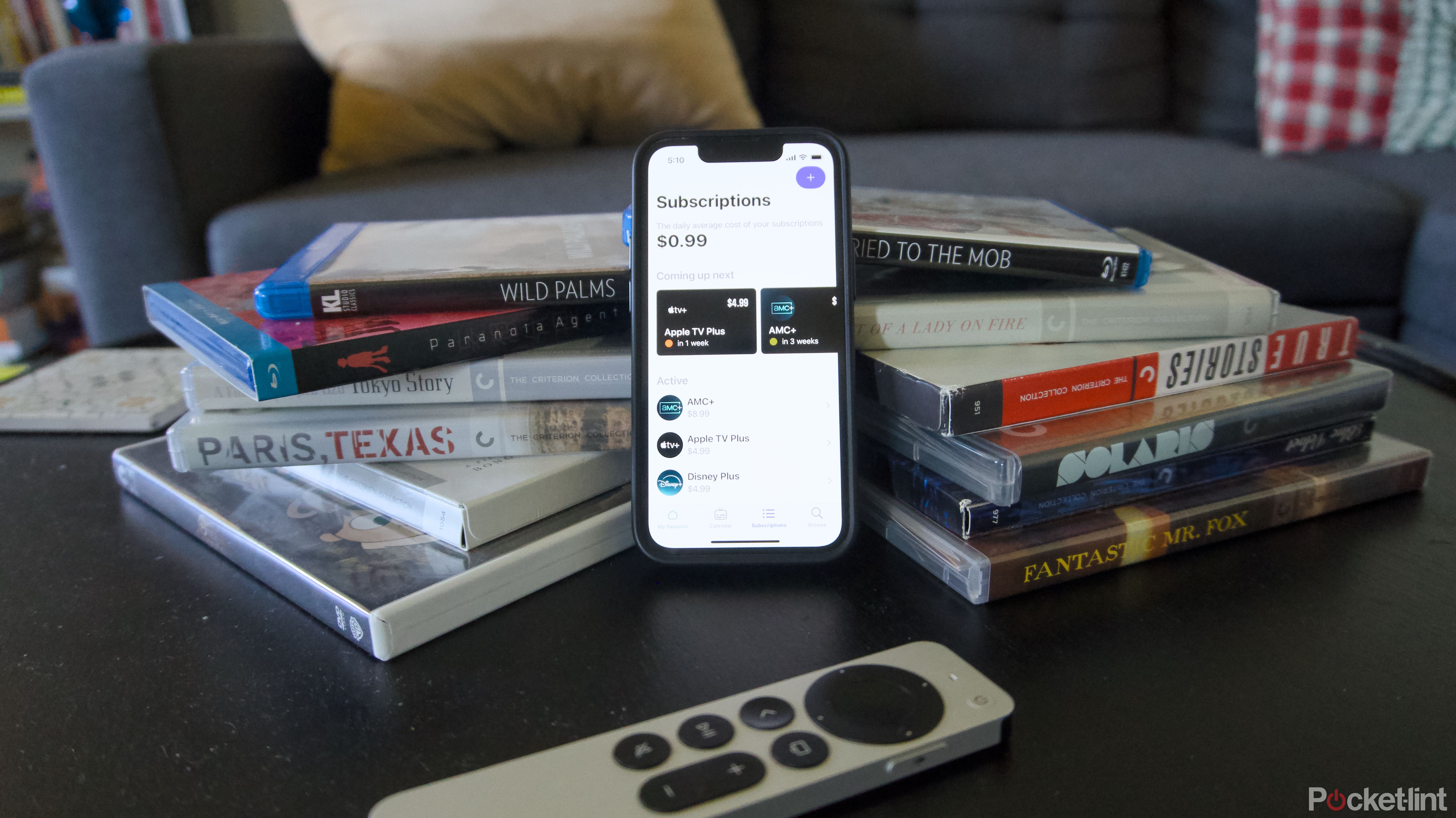 An iPhone 13 mini showing the Seasons app on a stack of Blu-rays.