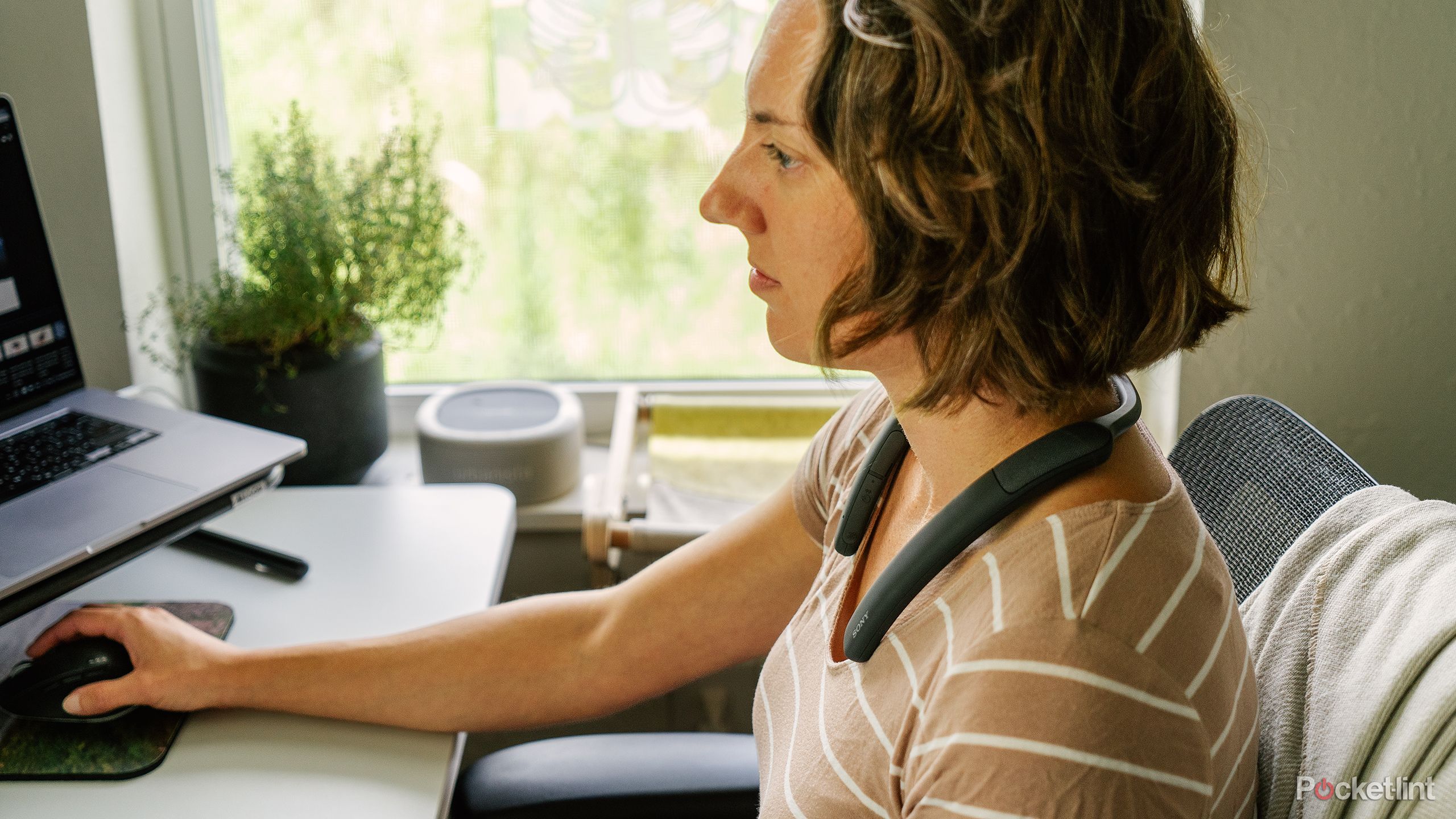 A woman sits at a desk with the Sony SRS-NB10 Wireless Neckband on her neck.