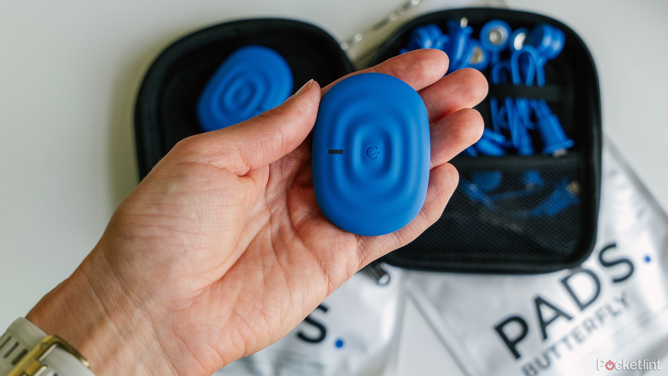 A hand holds a PowerDot pod above the PowerDot kit with packs of pads.