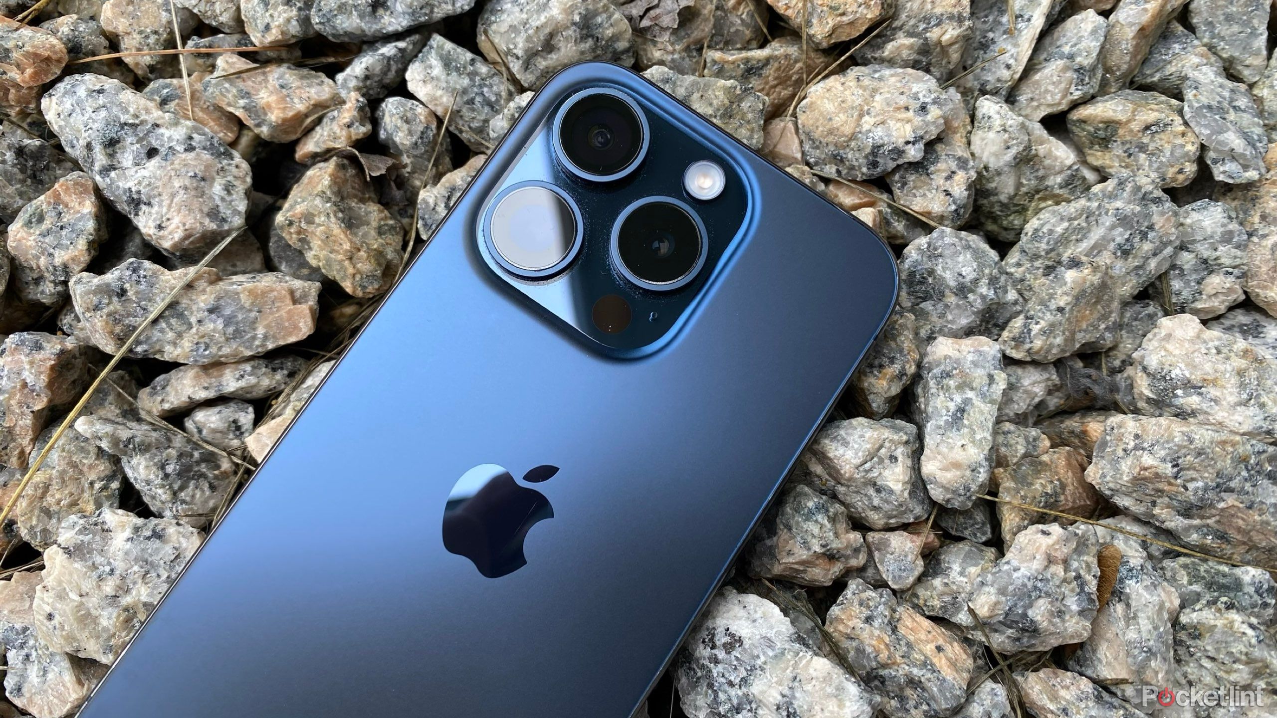A blue iPhone 15 Pro resting on gravel.