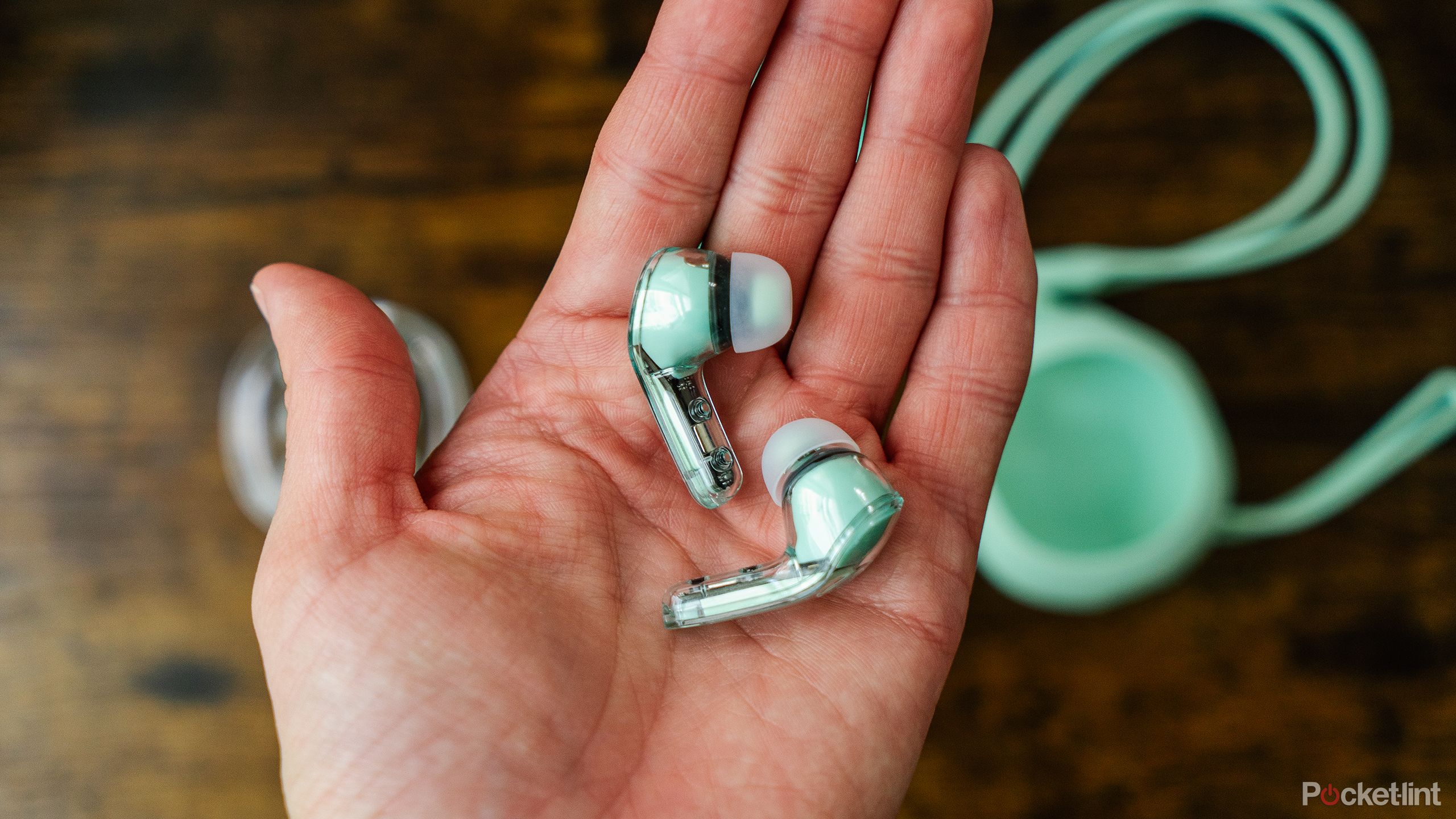 A hand holds the Acefast Crystal (2) T8 earbuds above its accessories on a wood table. 