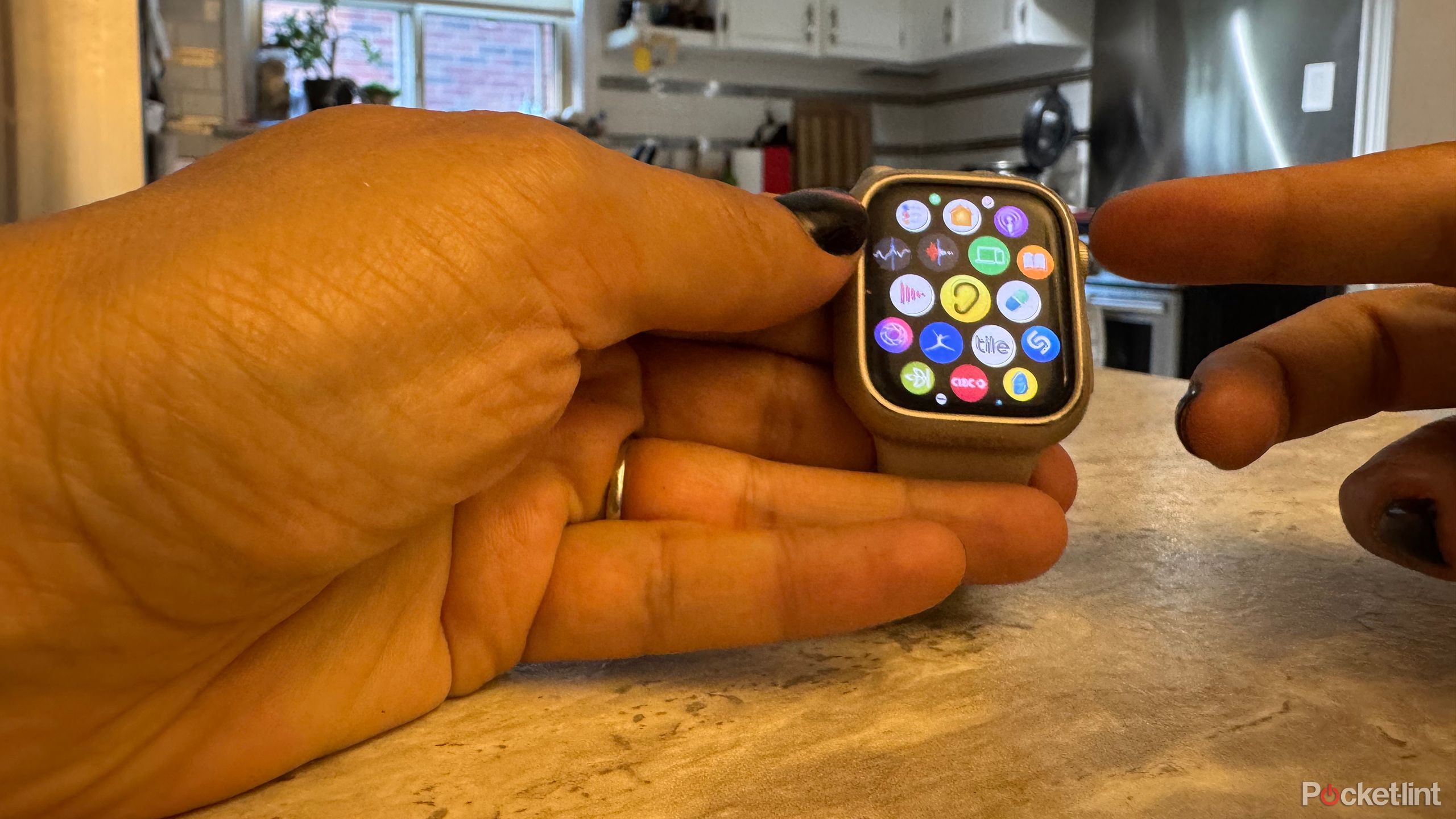 An Apple Watch in hand with a finger pressing the Digital Crown