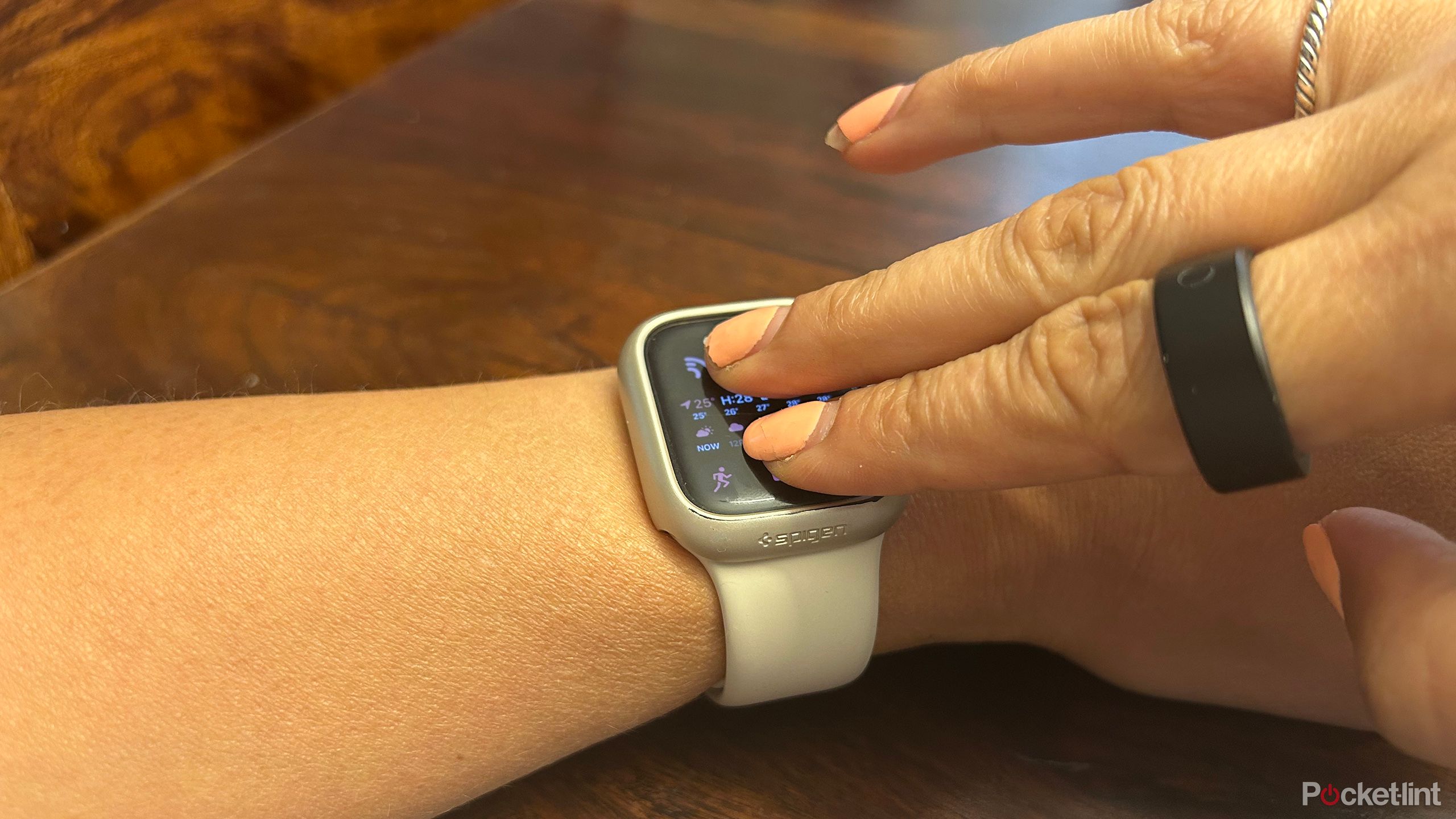 An Apple Watch on a wrist with two fingers of the other hand over the screen