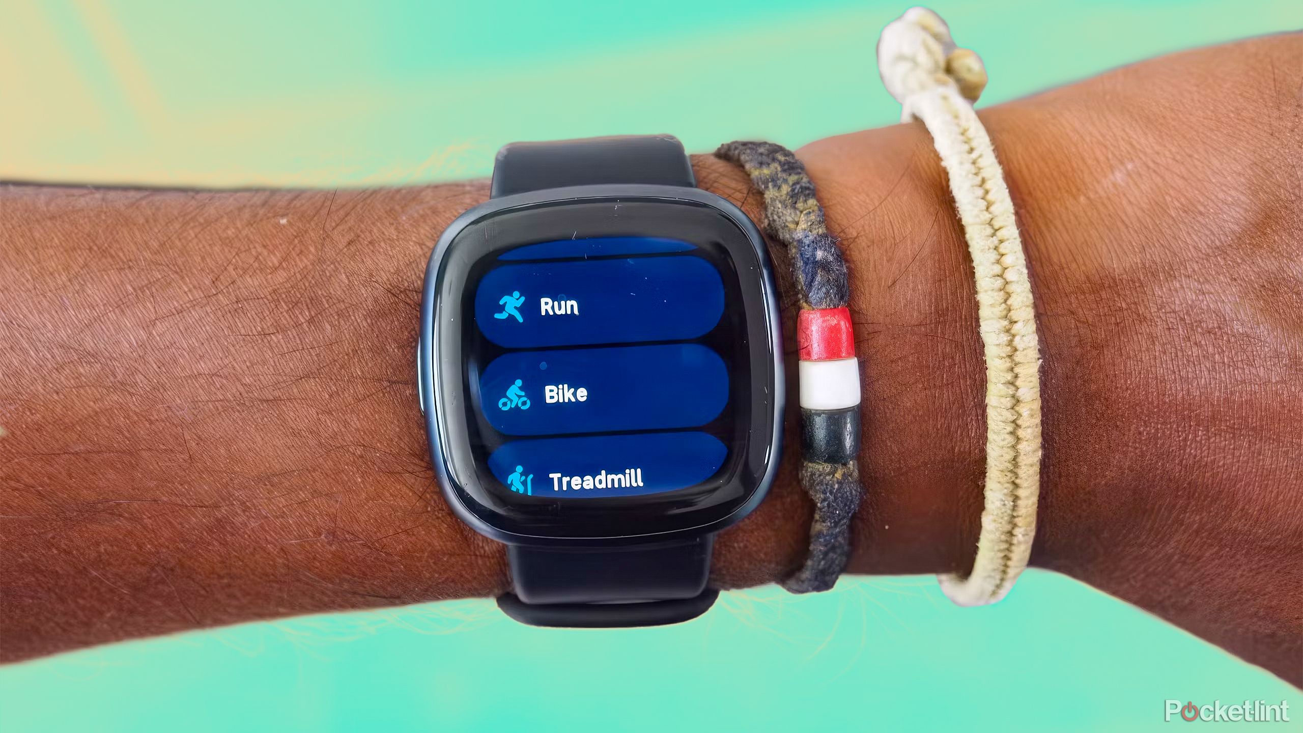 A wrist with the Fitbit Versa 4 against a yellow and mint green background. 