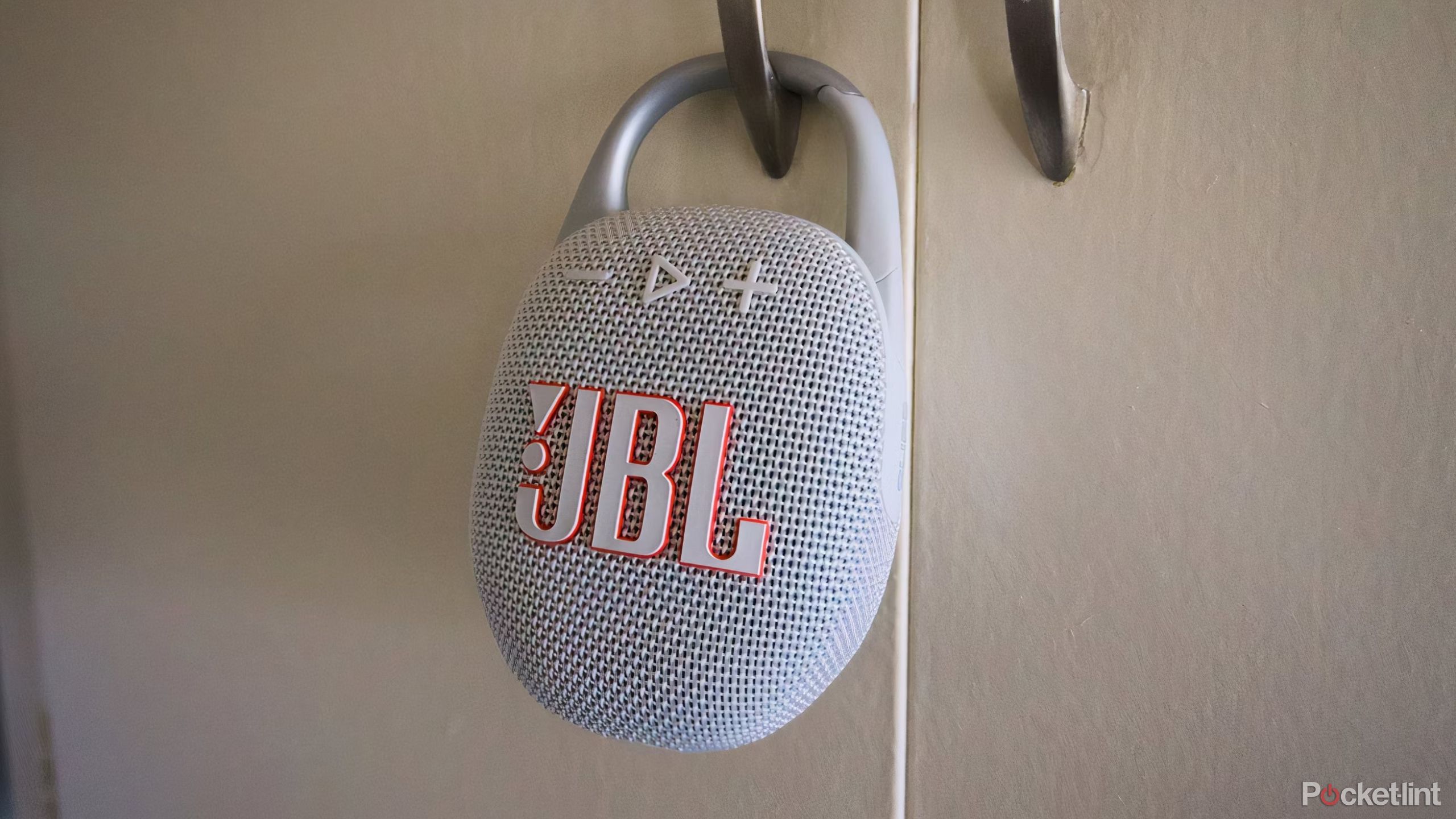 A JBL Clip 5 speaker clipped onto a kitchen cabinet door.