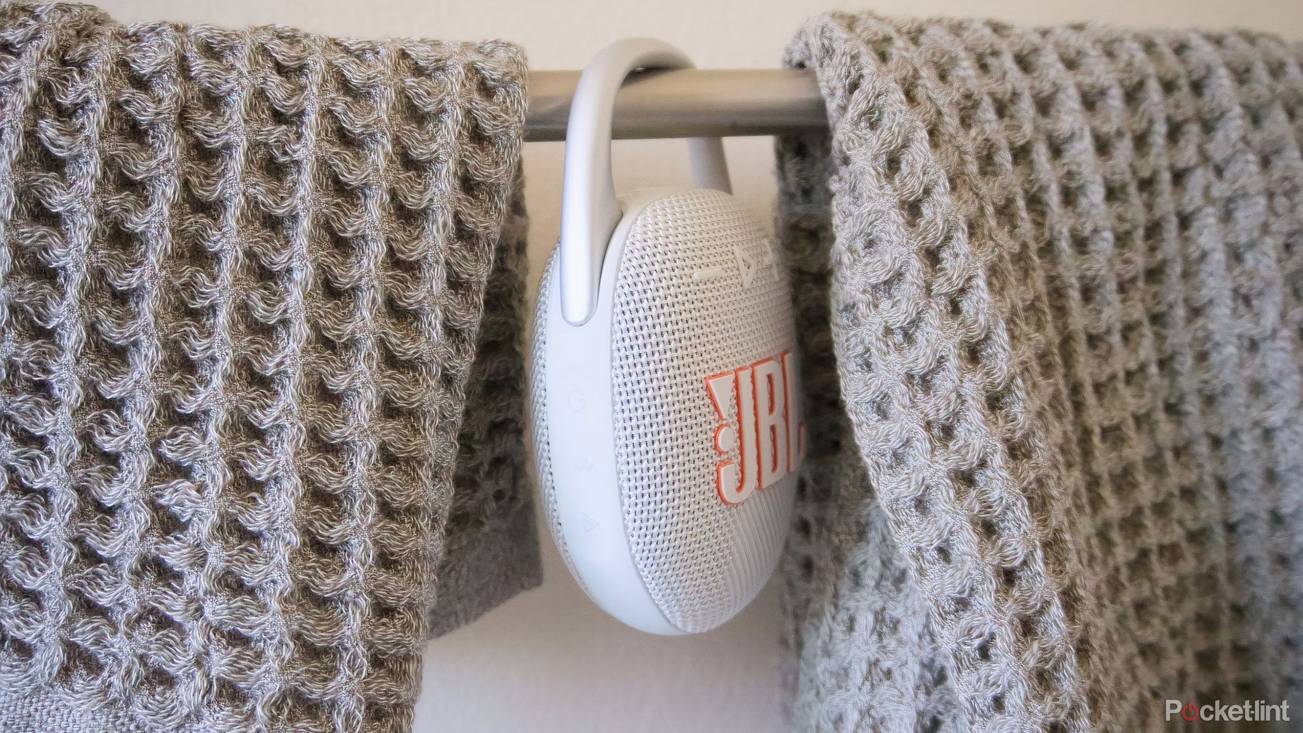 A JBL Clip 5 Bluetooth speaker hanging between hand towels.