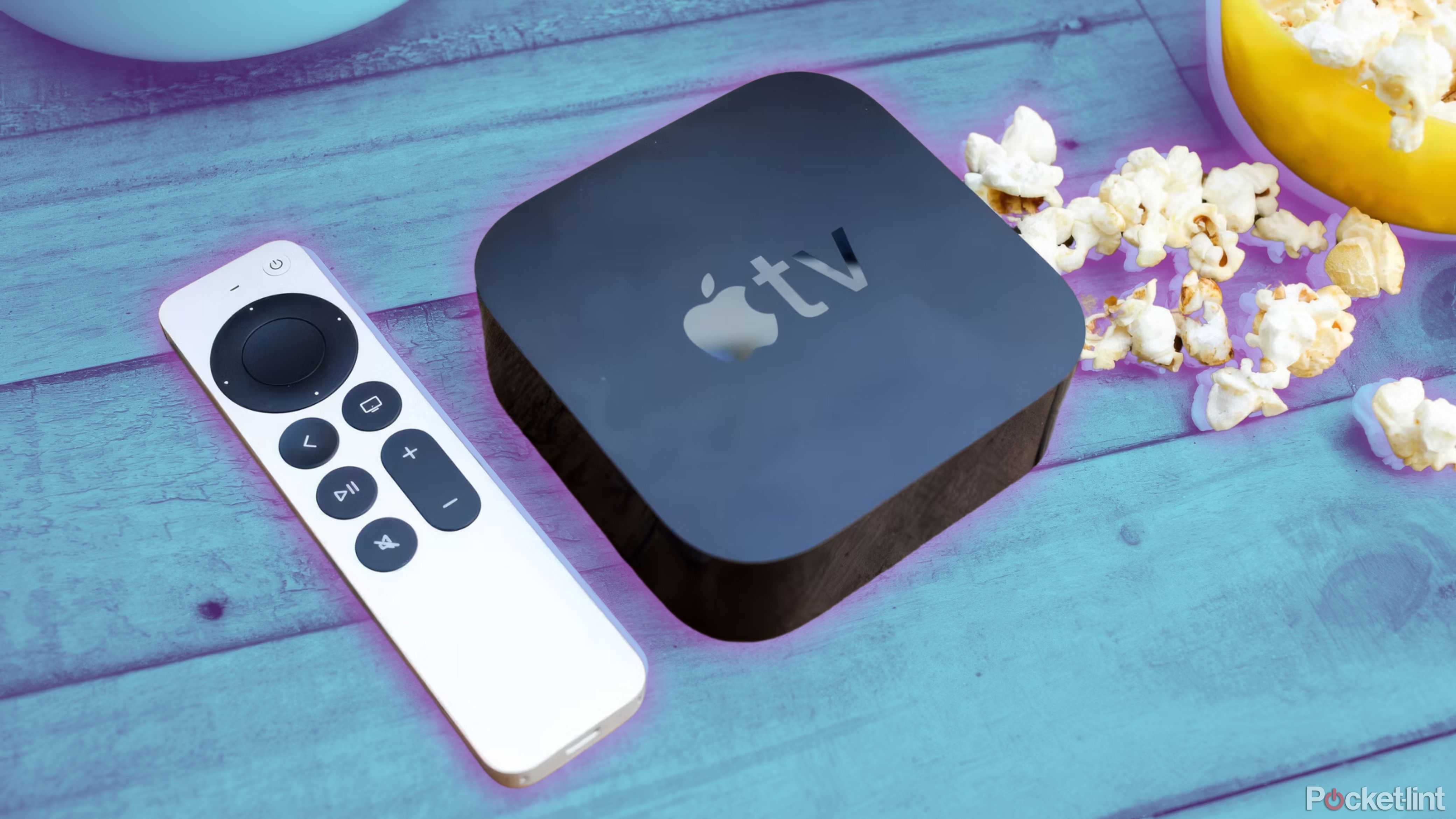 An Apple TV remote and box sit on a wood table next to popcorn.