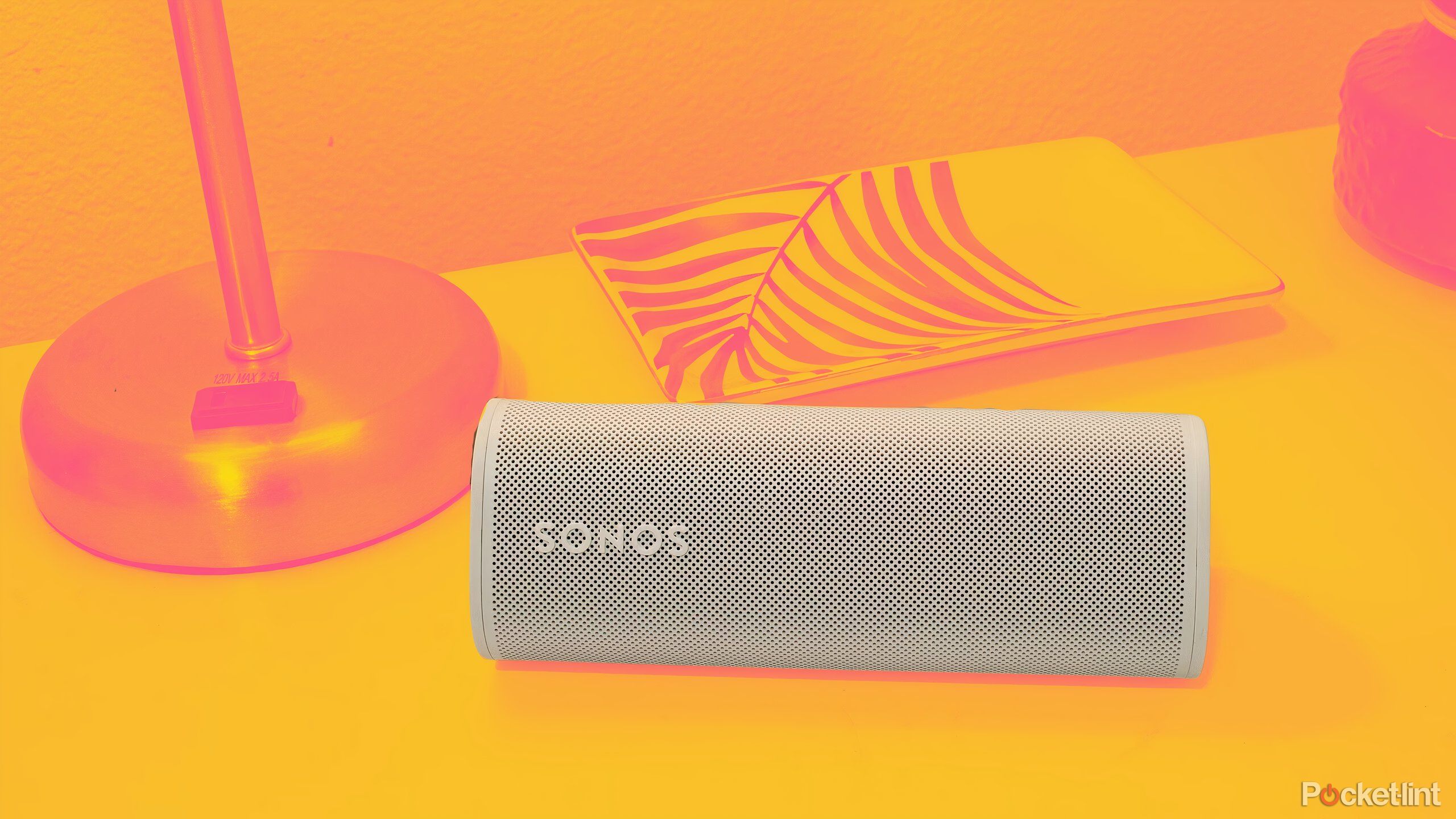 The Sonos Roam 2 sideways on a night stand colored with a golden yellow background.