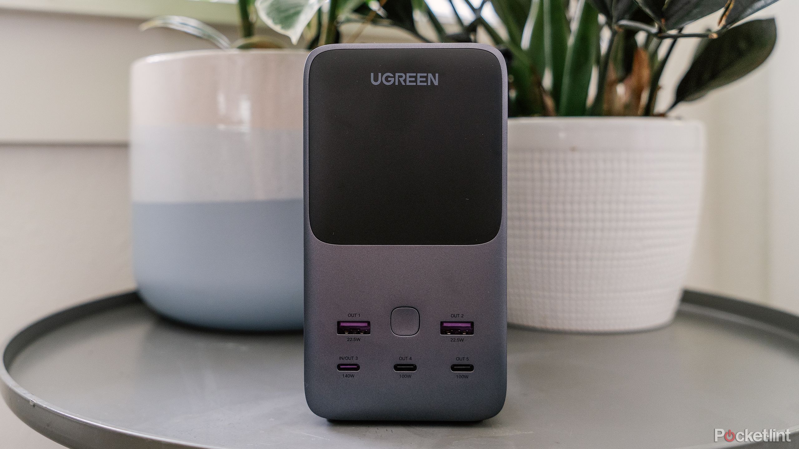 The Ugreen 300W 48000mAh Power Bank on a table in front of potted plants. 