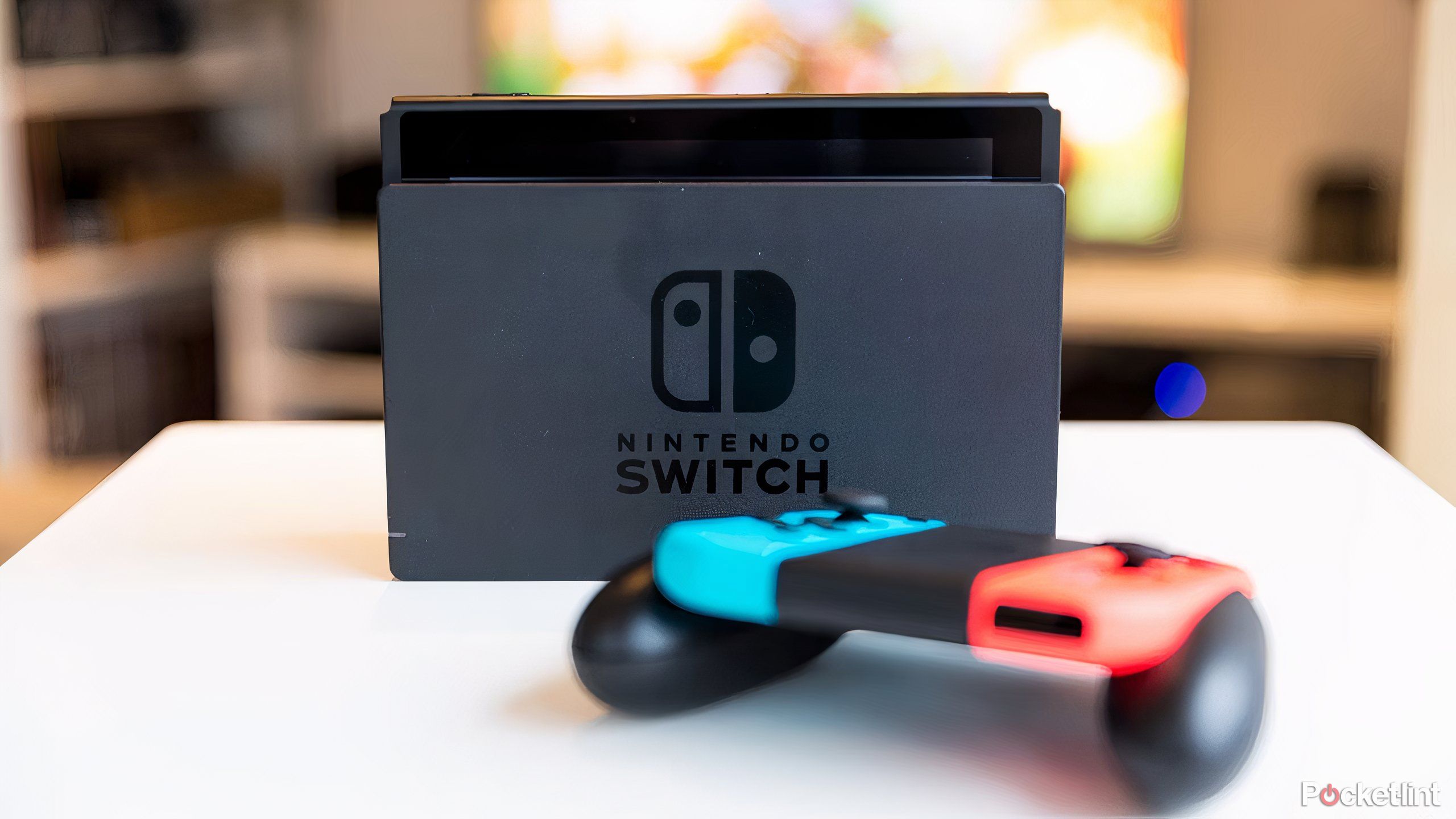 A Nintendo Switch in the Nintendo Switch charging dock, with a controller in the foreground