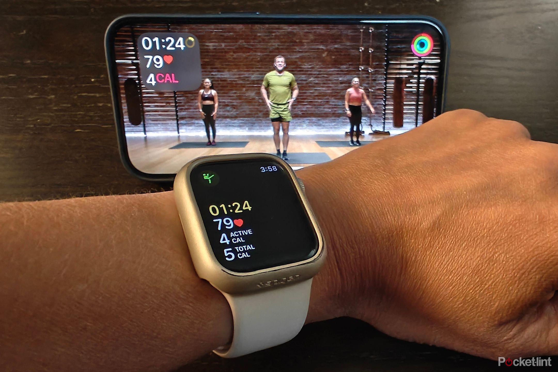 Um Apple Watch na frente de um iPhone, com o telefone mostrando um treino Apple Fitness+ e o relógio monitorando-o.