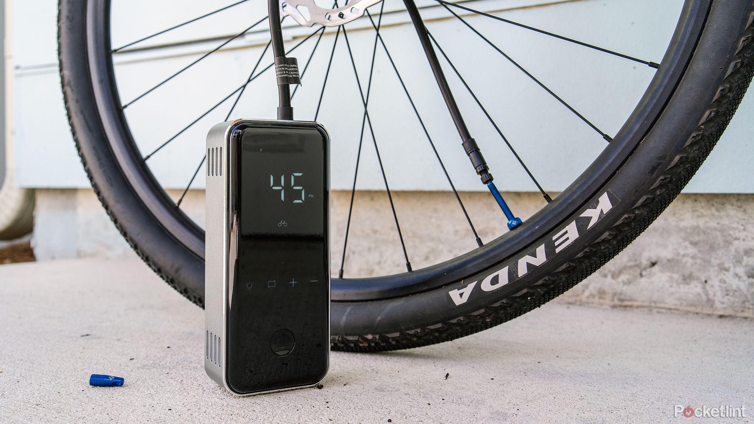 The Denvix Portable Air Compressor sits next to a bike tire on a concrete pad. 