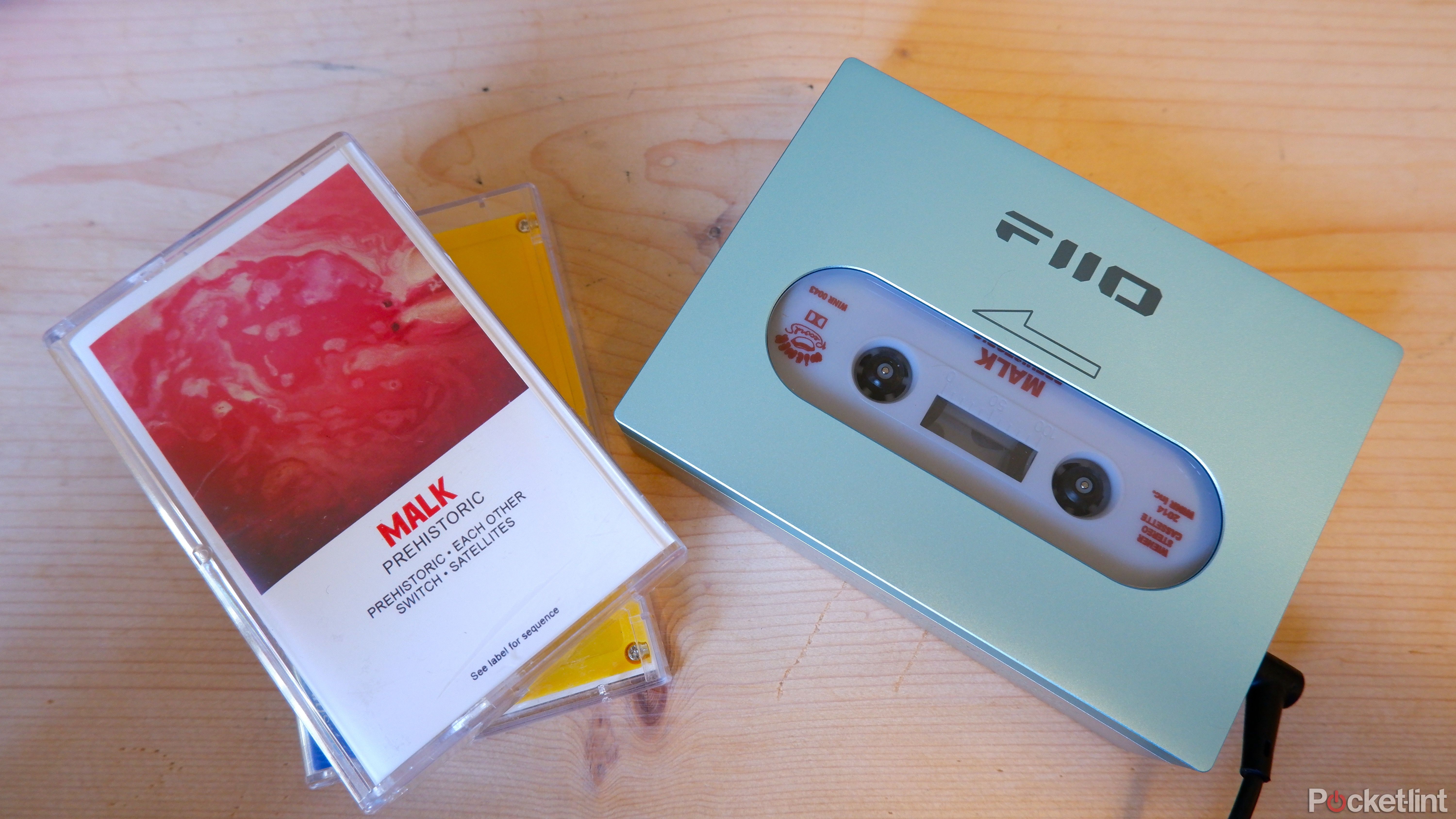 The Fiio CP13 on a wooden table next to two cassette tape cases