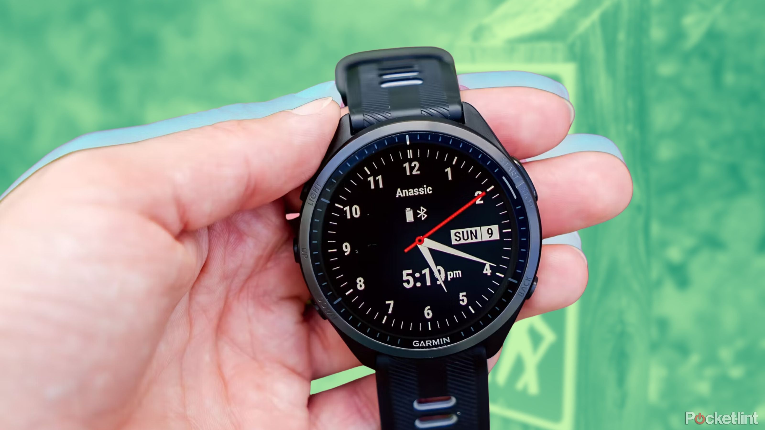 A hand holding the Garmin Forerunner 965 with an analog watch face. 