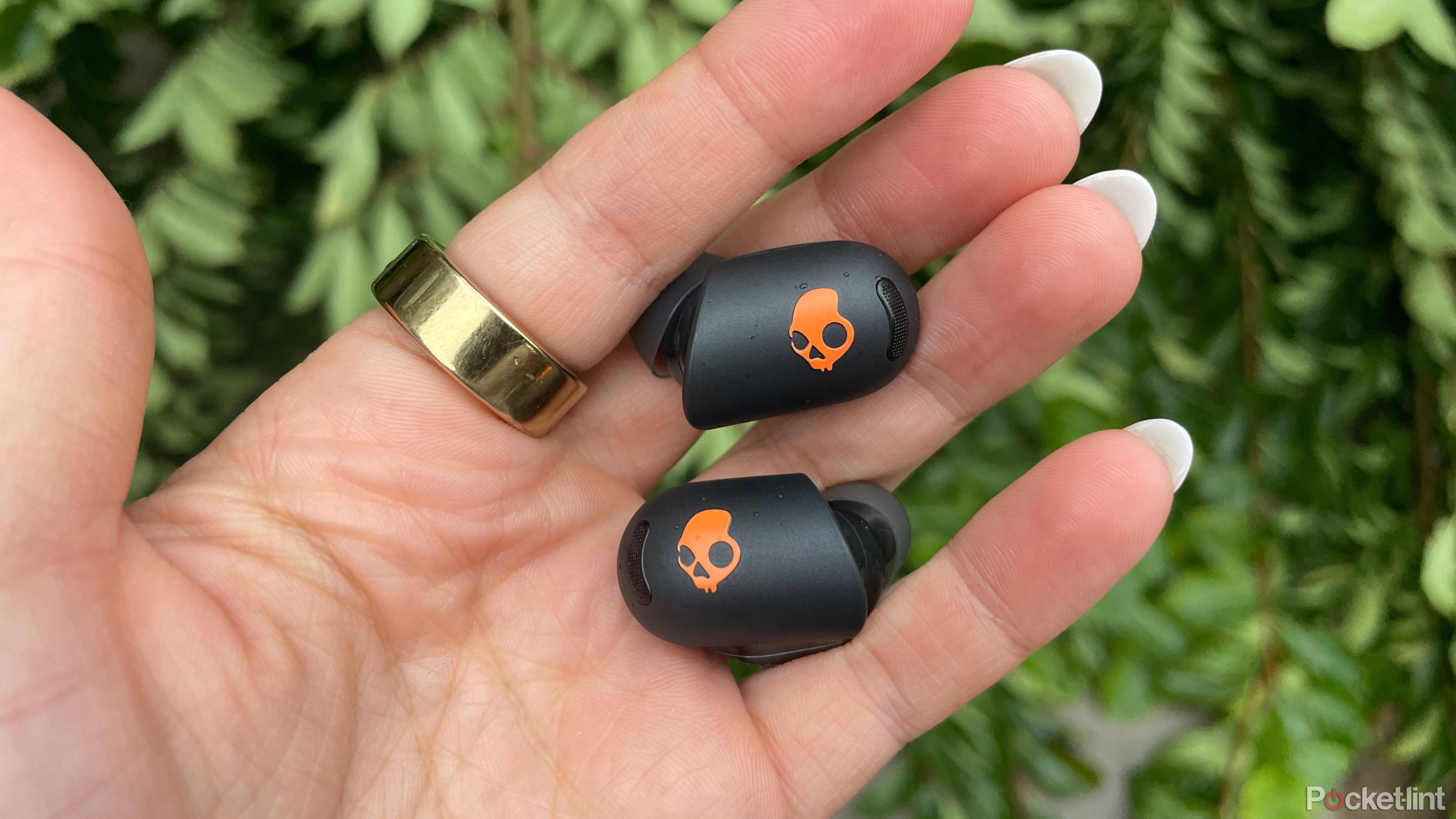 A person holding the Skullcandy Sesh ANC Active earbuds with a gold ring on. 