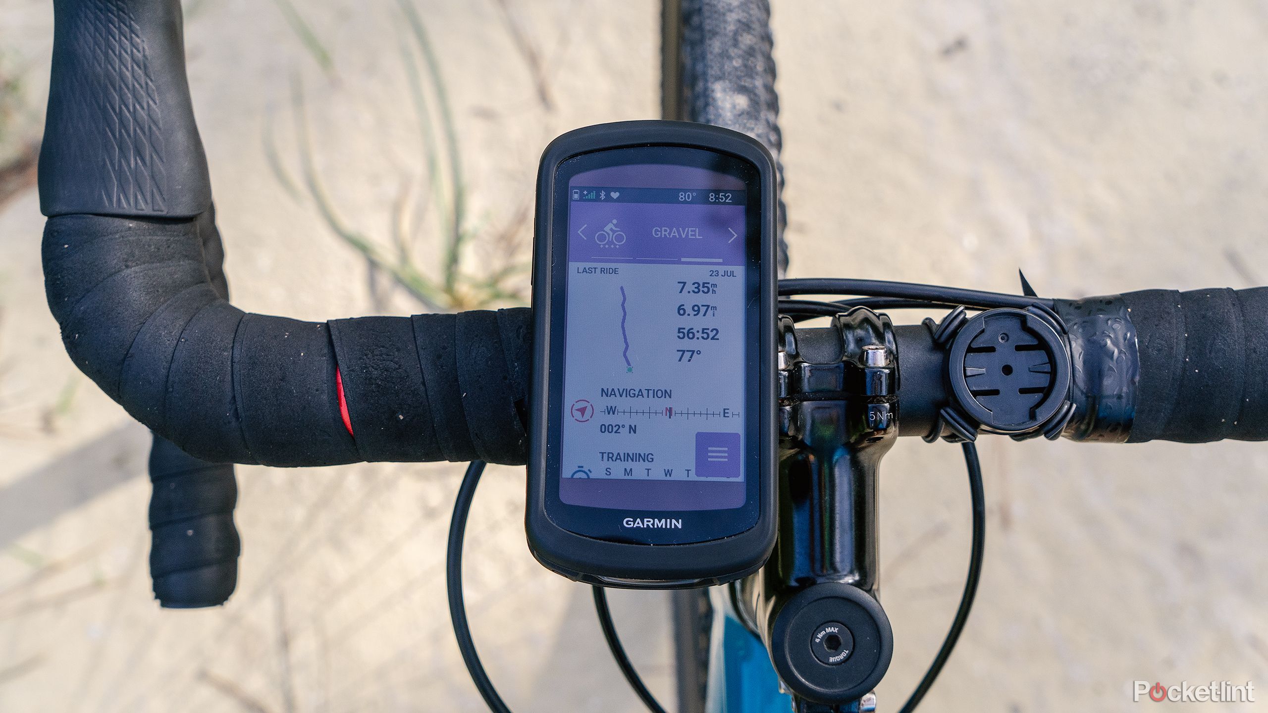 The Garmin Edge 1040 Solar sits on bike handlebars over a sandy road. 