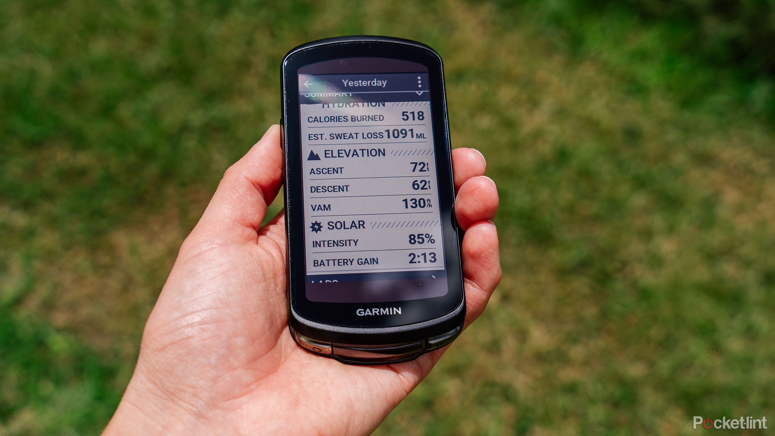 A hand holds the Garmin Edge 1040 Solar above blurred out grass. 