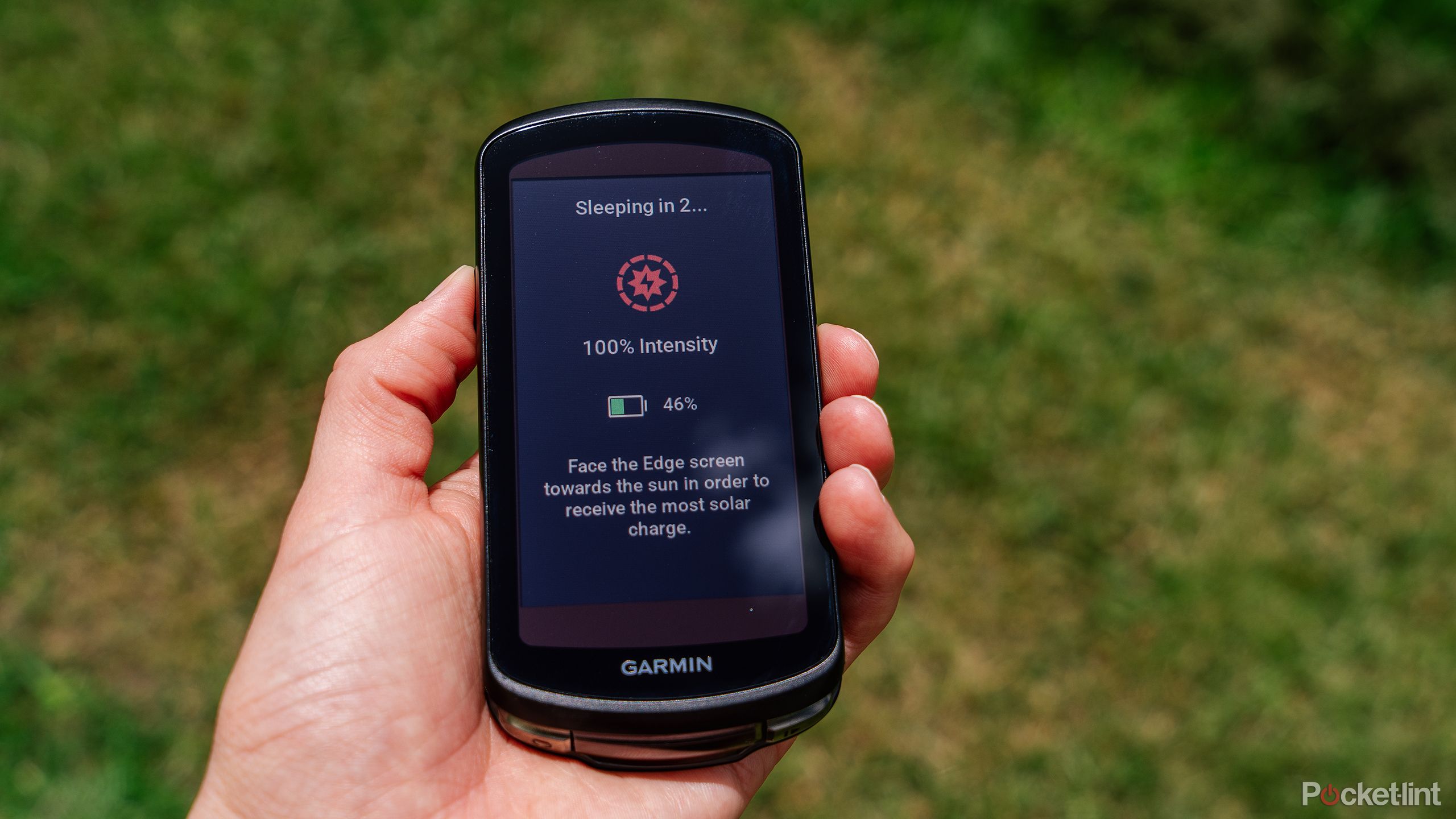 A hand holds the Garmin Edge 1040 Solar over blurred grass. 