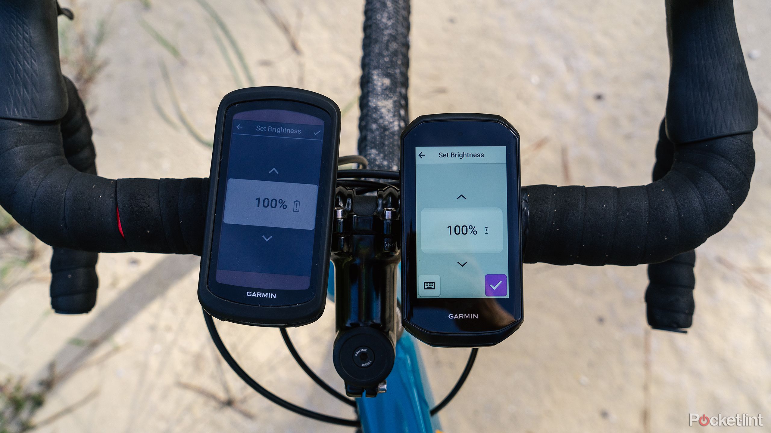 The Garmin Edge 1040 Solar and Garmin Edge 1050 are mounted on the handlebars of a bike on a sandy road. 