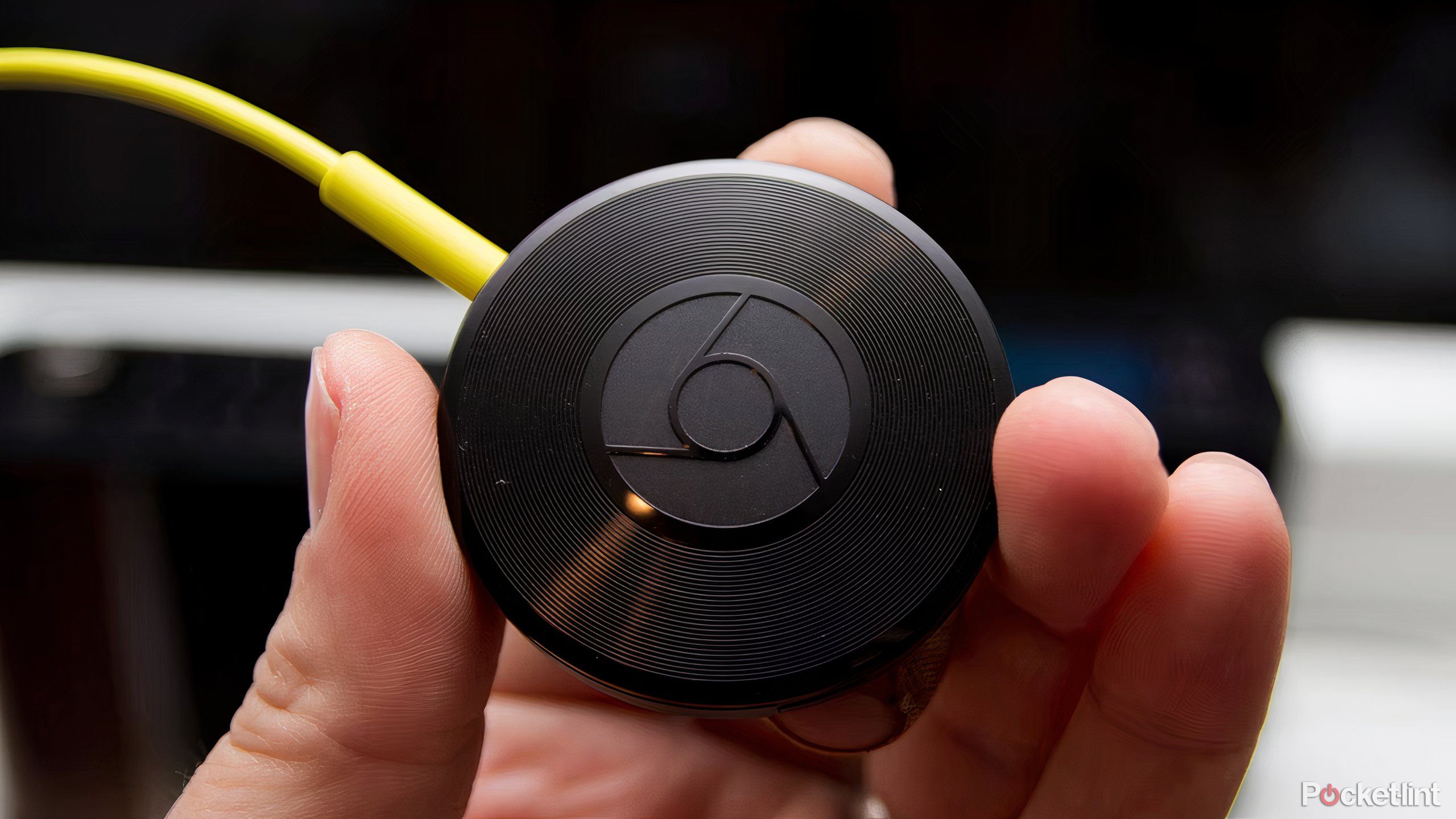 A hand holding a vinyl record-hsaped Google Chromecast Audio.