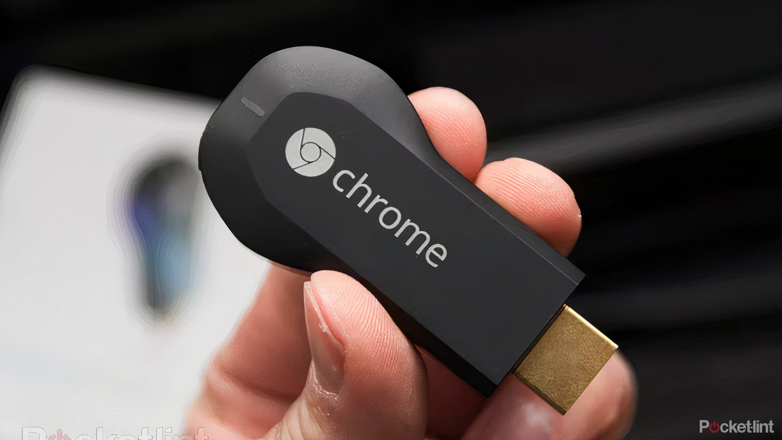 A hand holding a first generation Google Chromecast.